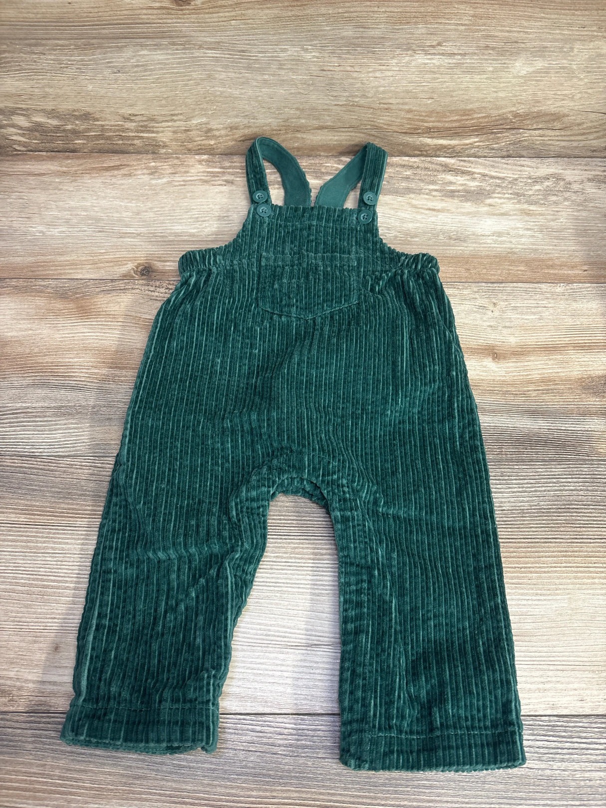 Dark green corduroy baby overalls with adjustable shoulder straps laid on wooden background
