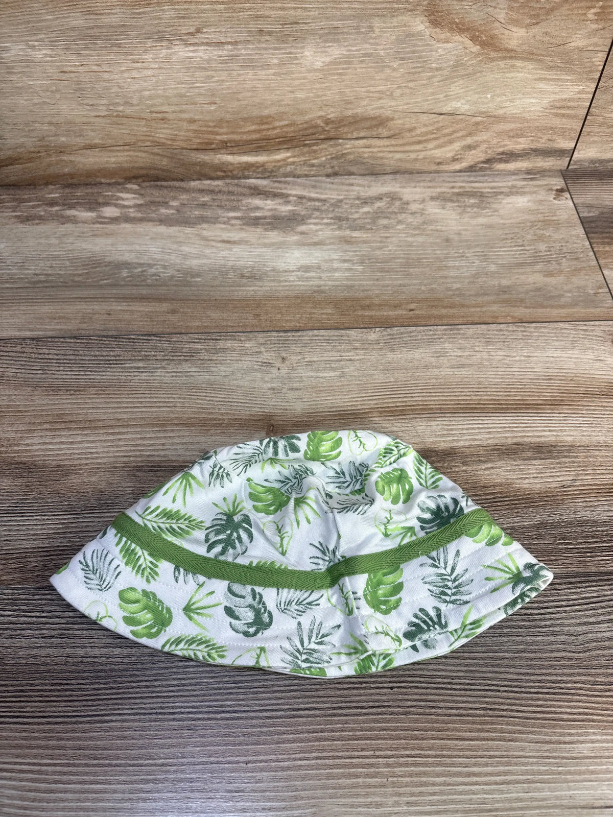 Top view of white tropical bamboo bucket hat, size 9 months, showcasing green leaf print on a wood background