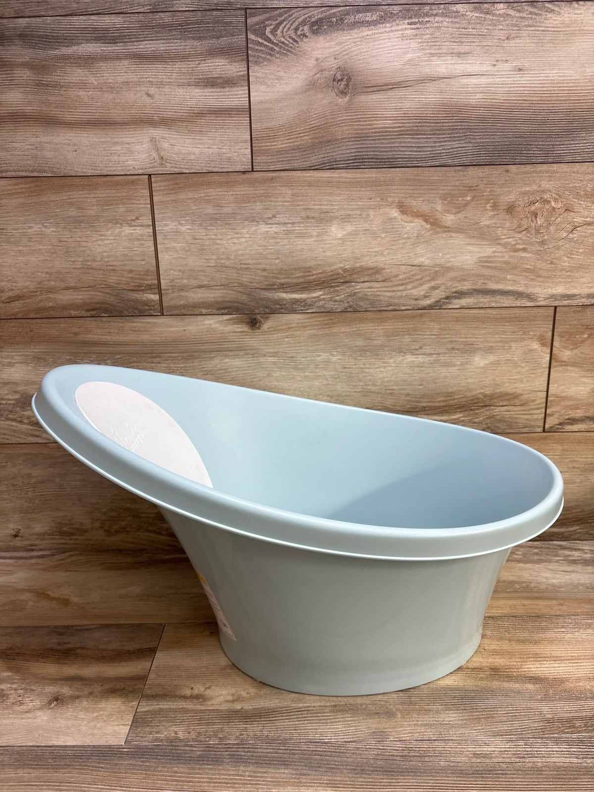 Side view of BEABA by Shnuggle baby bathtub showcasing sloped ergonomic interior and white headrest with wood plank background