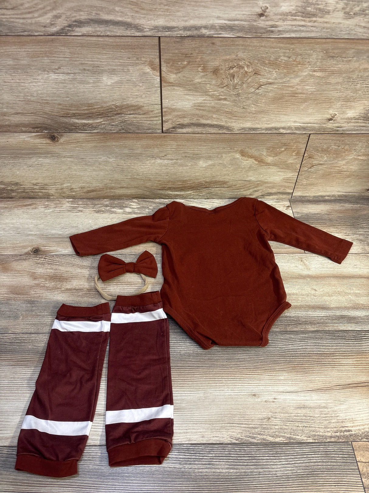 Flat lay of brown baby bodysuit with matching leg warmers with white stripes and bow headband on wood background