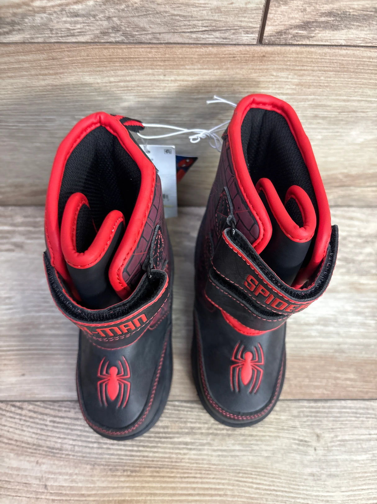 Children's black and red Spider-Man boots with spider logo and Velcro straps on wooden floor