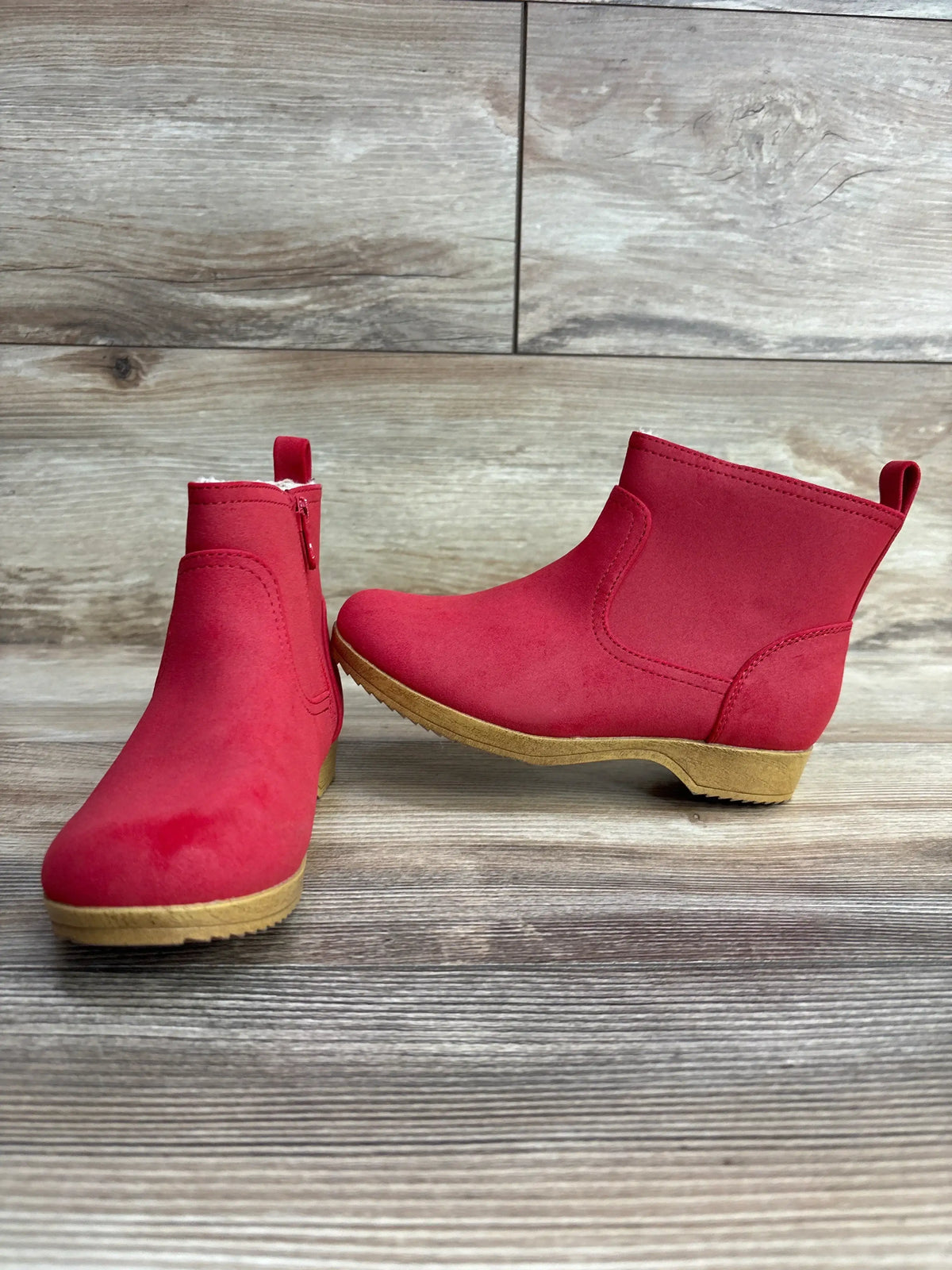 Pair of red toddler ankle boots with side zippers on wooden background
