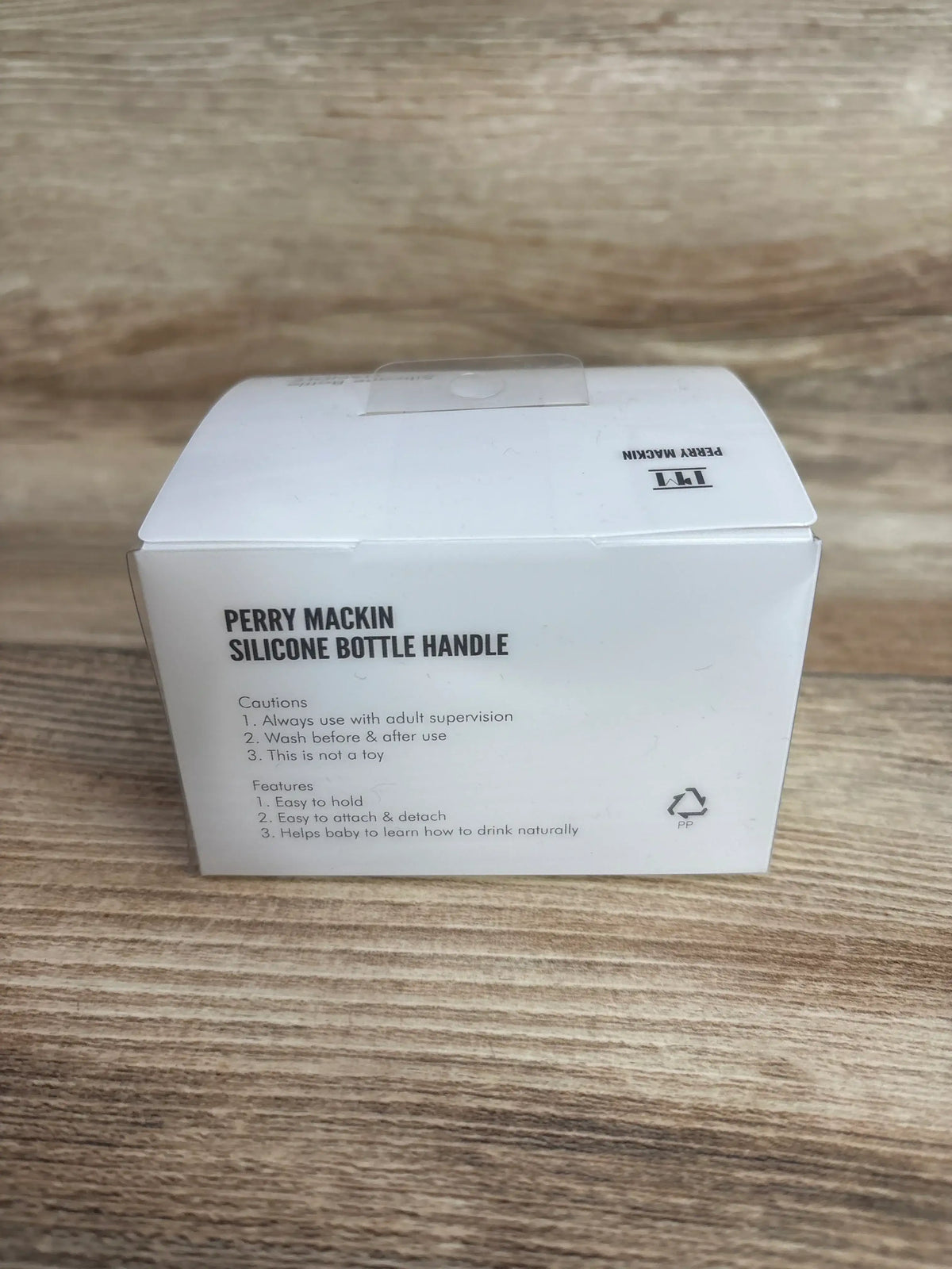 Perry Mackin silicone bottle handle box on wooden surface, baby feeding accessory.