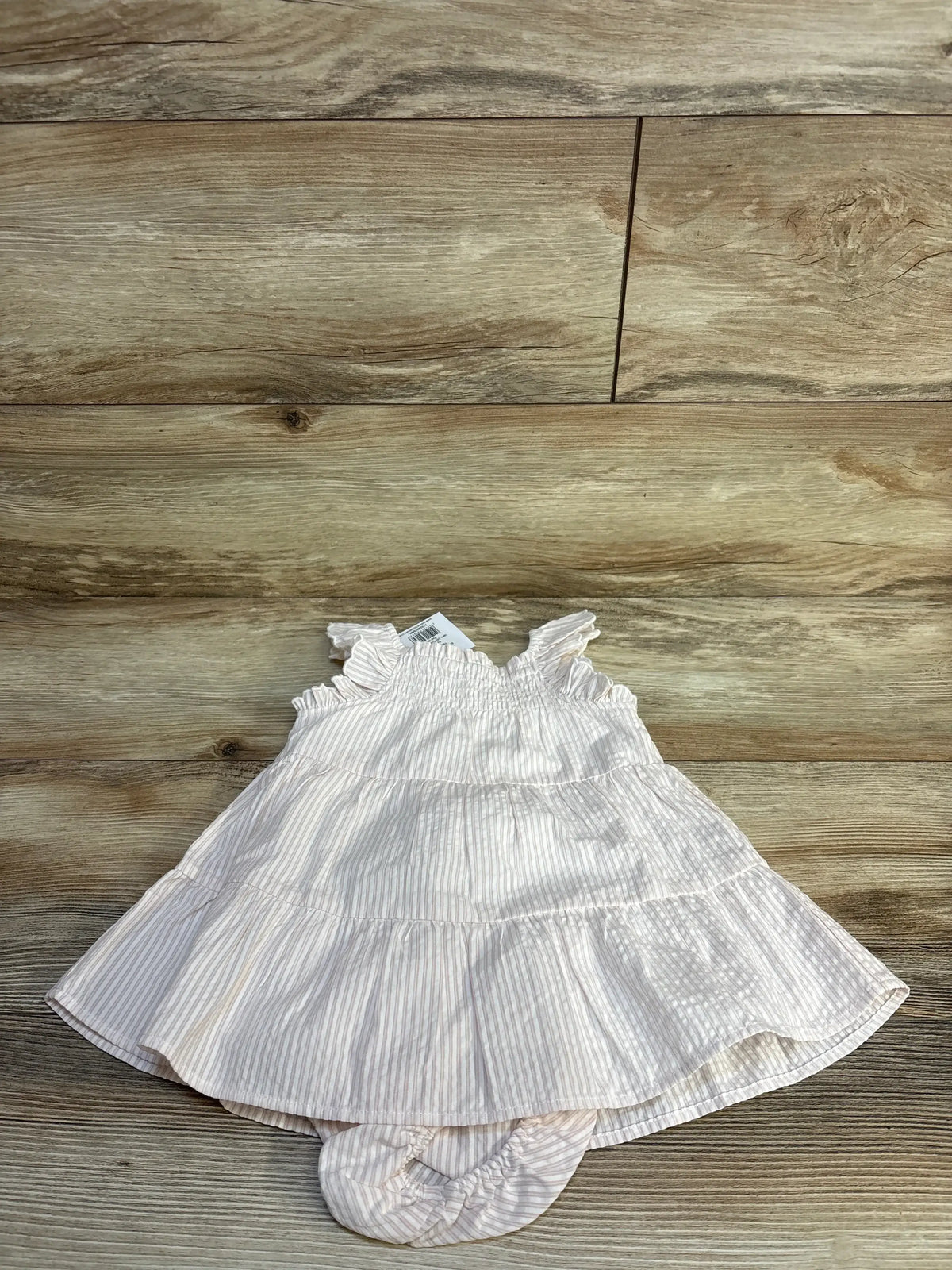 Flat lay of 2-piece frill-sleeve tiered baby dress and matching bloomers, white with pale pink stripes, smocked bodice on wood floor