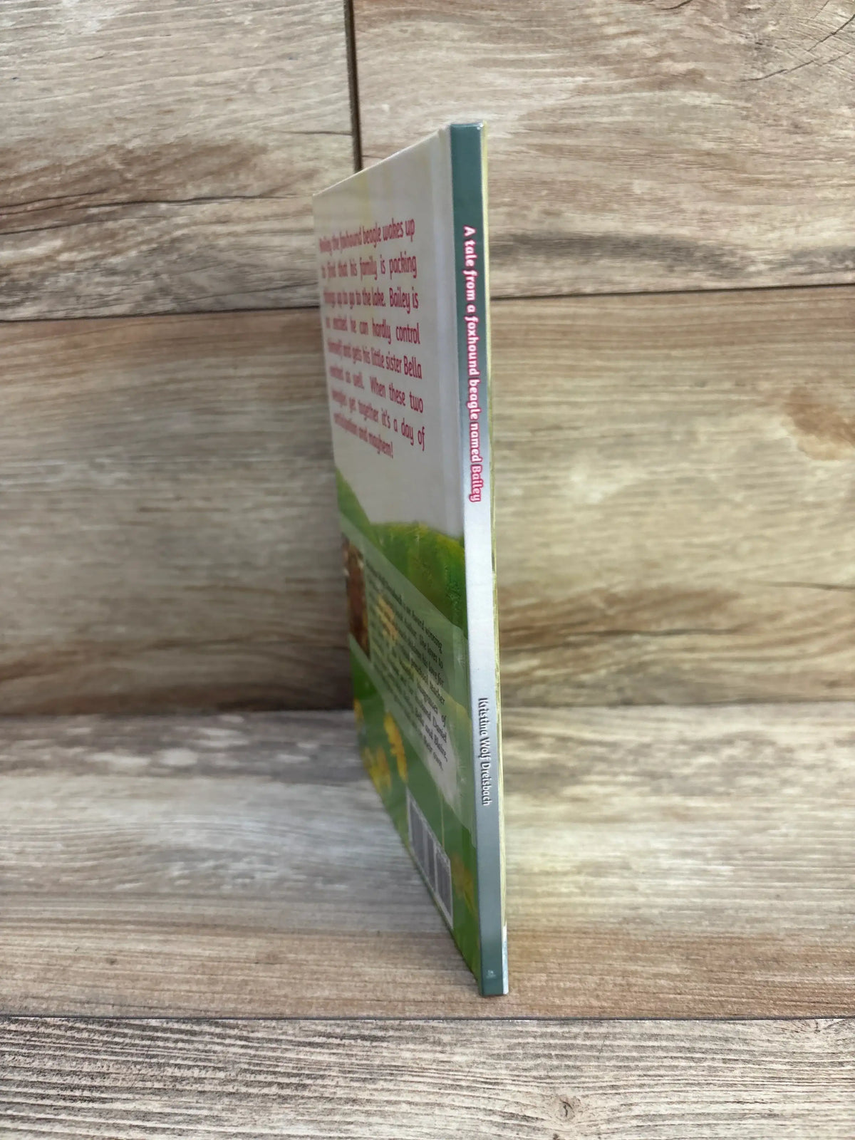 Side view of A Tale From A Foxhound Beagle Named Bailey hardcover book showing thin spine and illustrated back cover on wood tabletop