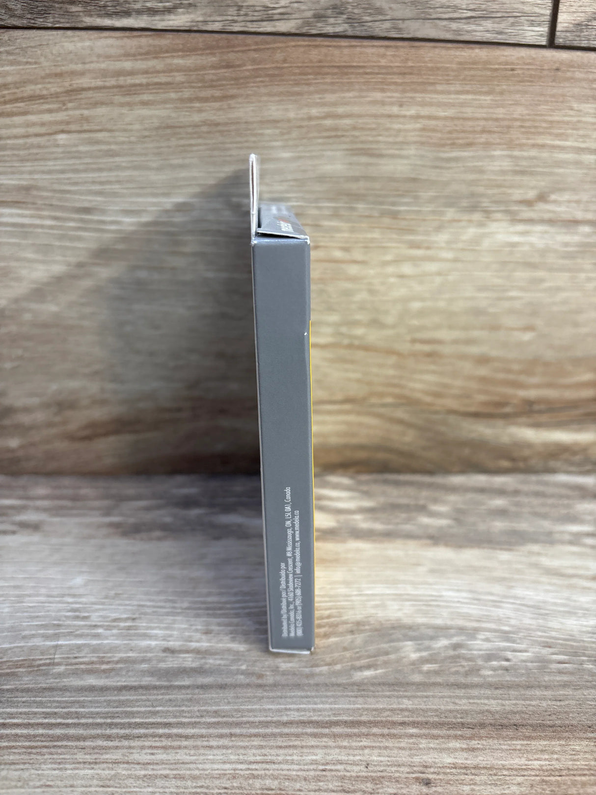 Side view of a small grey and yellow product box on a wooden surface with text on the side