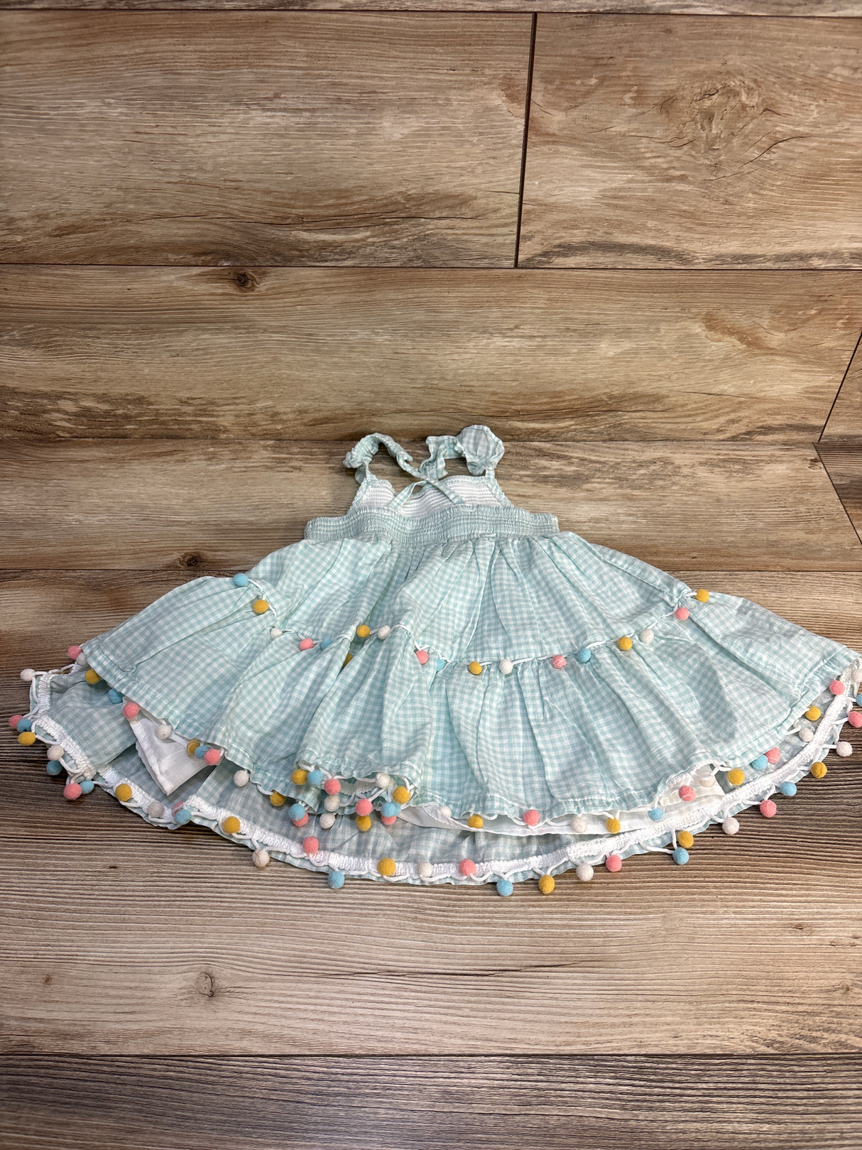 Light blue gingham baby dress with colorful pom-poms, perfect for summer outfits and resale shopping.