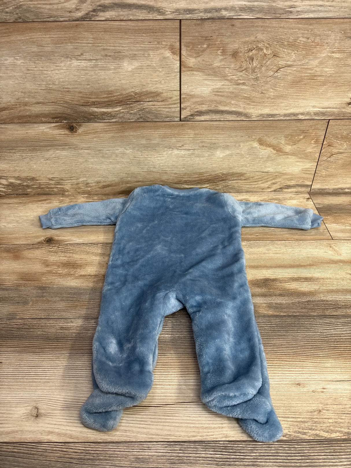 Blue fleece baby footed sleeper laid flat on wooden floor, long sleeves, cozy fabric