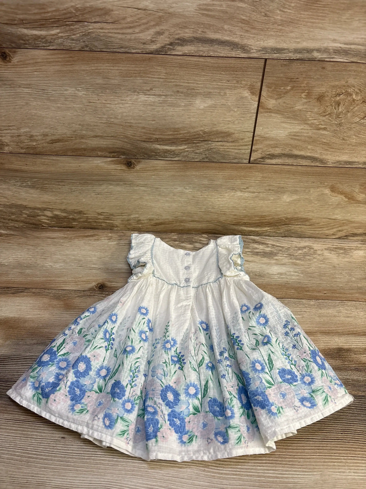 Front view of Haute Hippie floral sleeveless dress showcasing blue and pink flowers and gathered waist with wood floor background