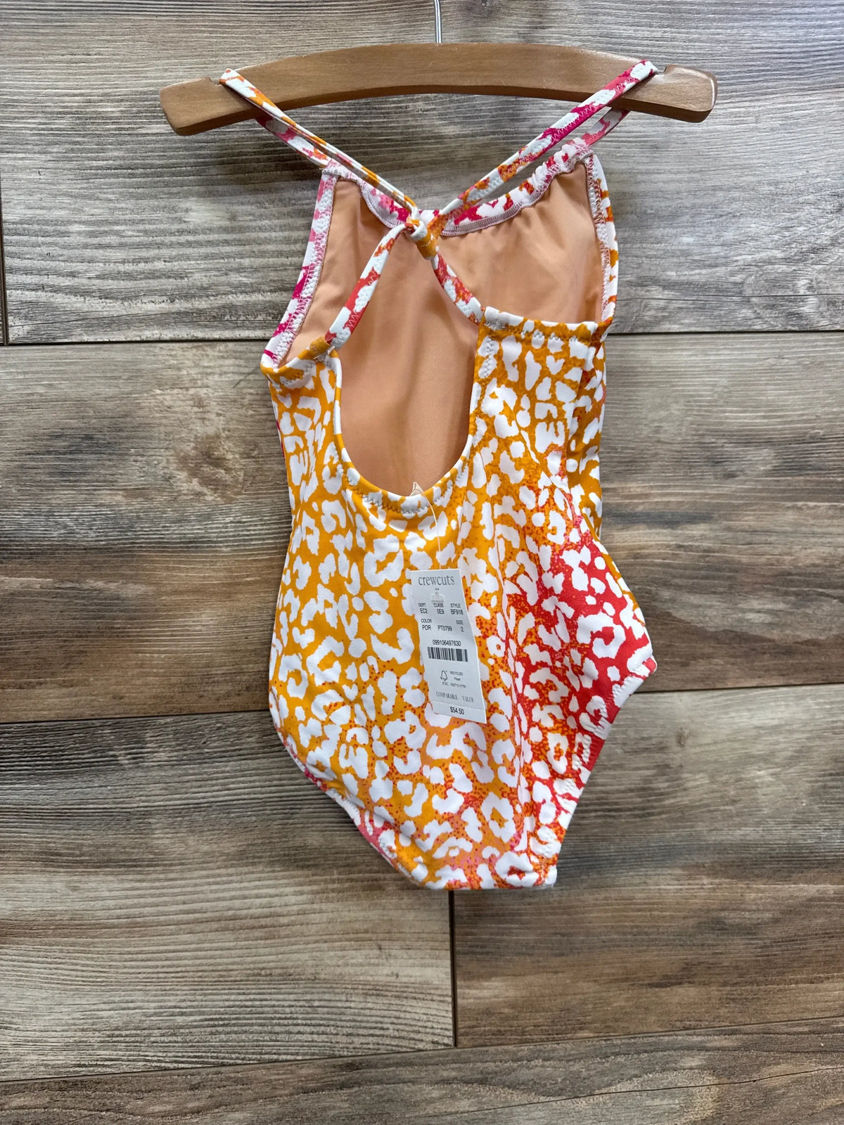 Back view of Crewcuts toddler one-piece leopard-print swimsuit with knotted cross-back straps on wooden hanger