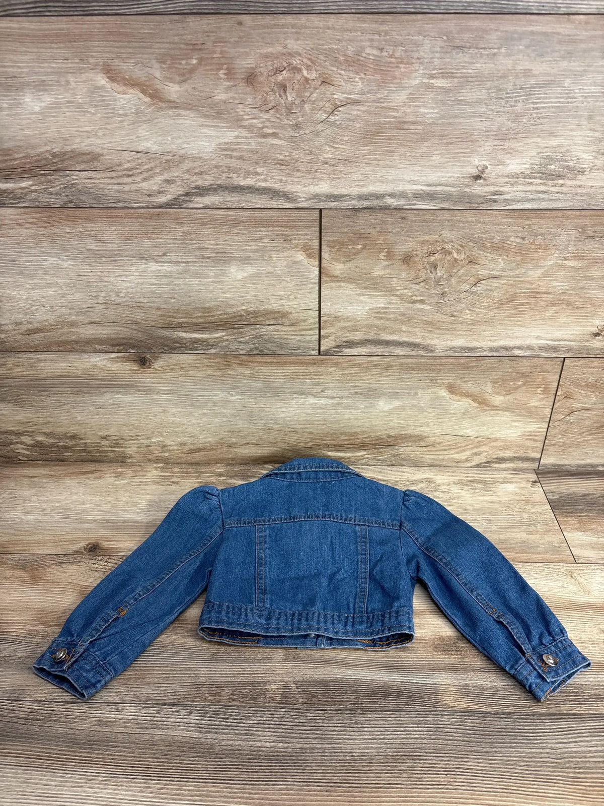 Back view of a blue denim child's jacket laid flat on wood floor
