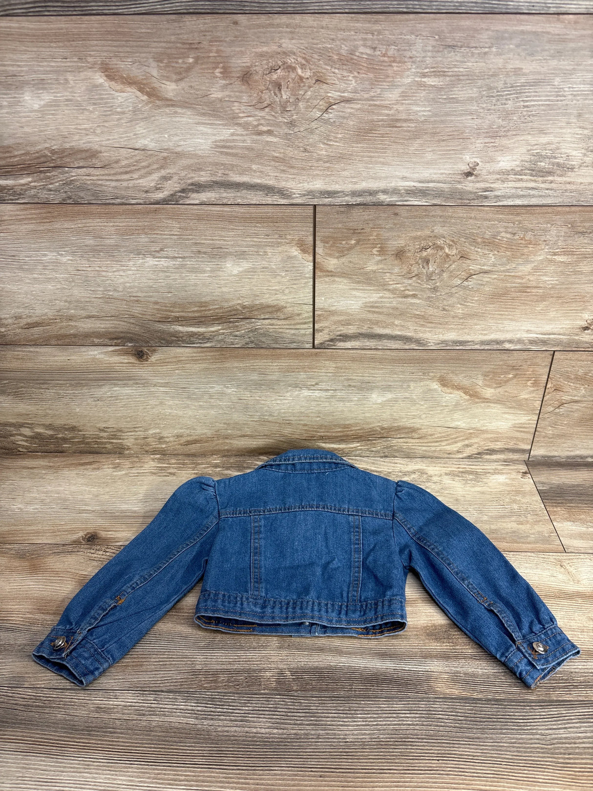 Back view of a blue denim child's jacket laid flat on wood floor
