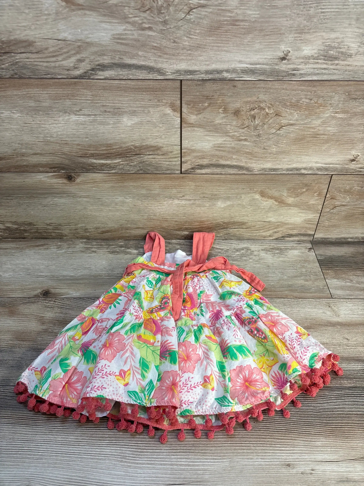 Floral baby dress with pink trim and tropical pattern on a wooden background