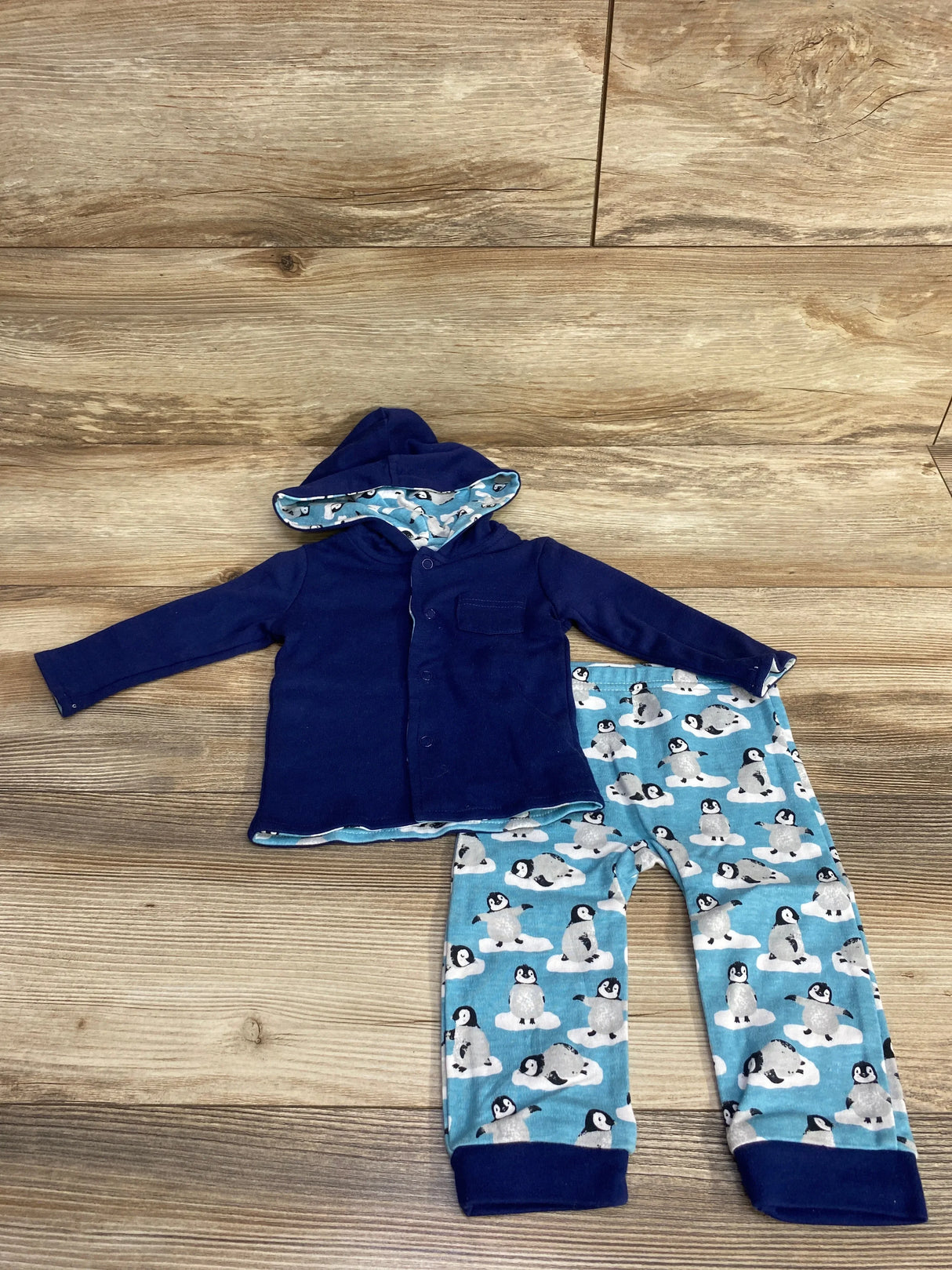 Flat-lay of Harry & Violet reversible navy button-up jacket and matching penguin-print pants on wooden floor