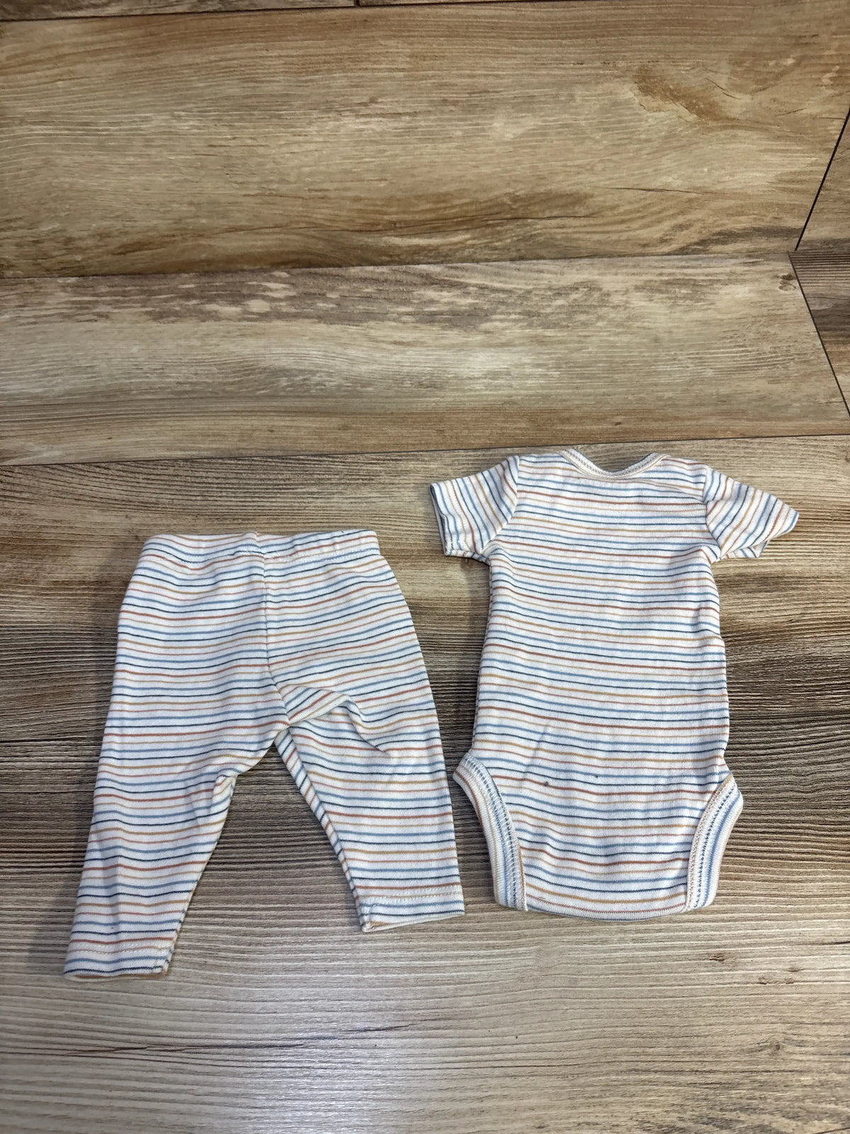 Top view of Just One You bodysuit and bottoms set showcasing white and blue stripes for preemie size on a wood background