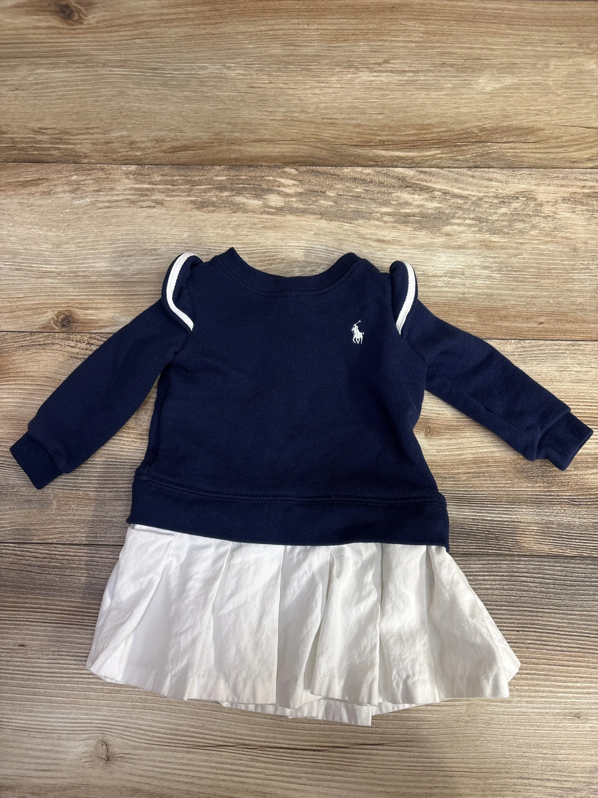 Navy blue long sleeve baby dress with white pleated skirt and embroidered logo on wooden background