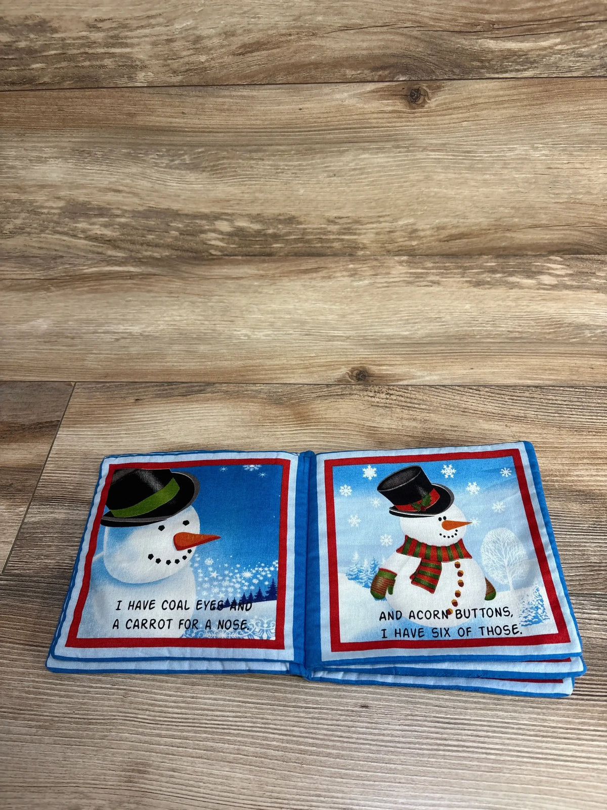 Open view of A Snowman Story soft book showing two snowmen with page text coal eyes, carrot nose, acorn buttons