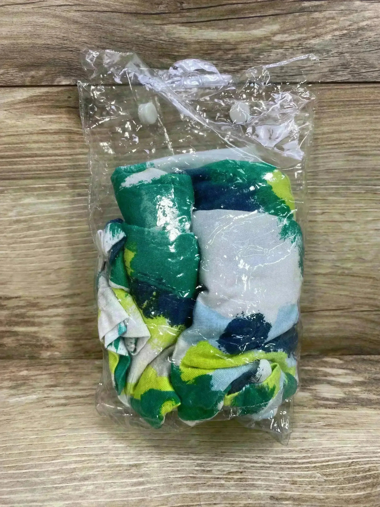Top view of Canopy Couture jersey stretch carseat cover in original sealed packaging showcasing green navy and yellow brush strokes print on wood plank floor