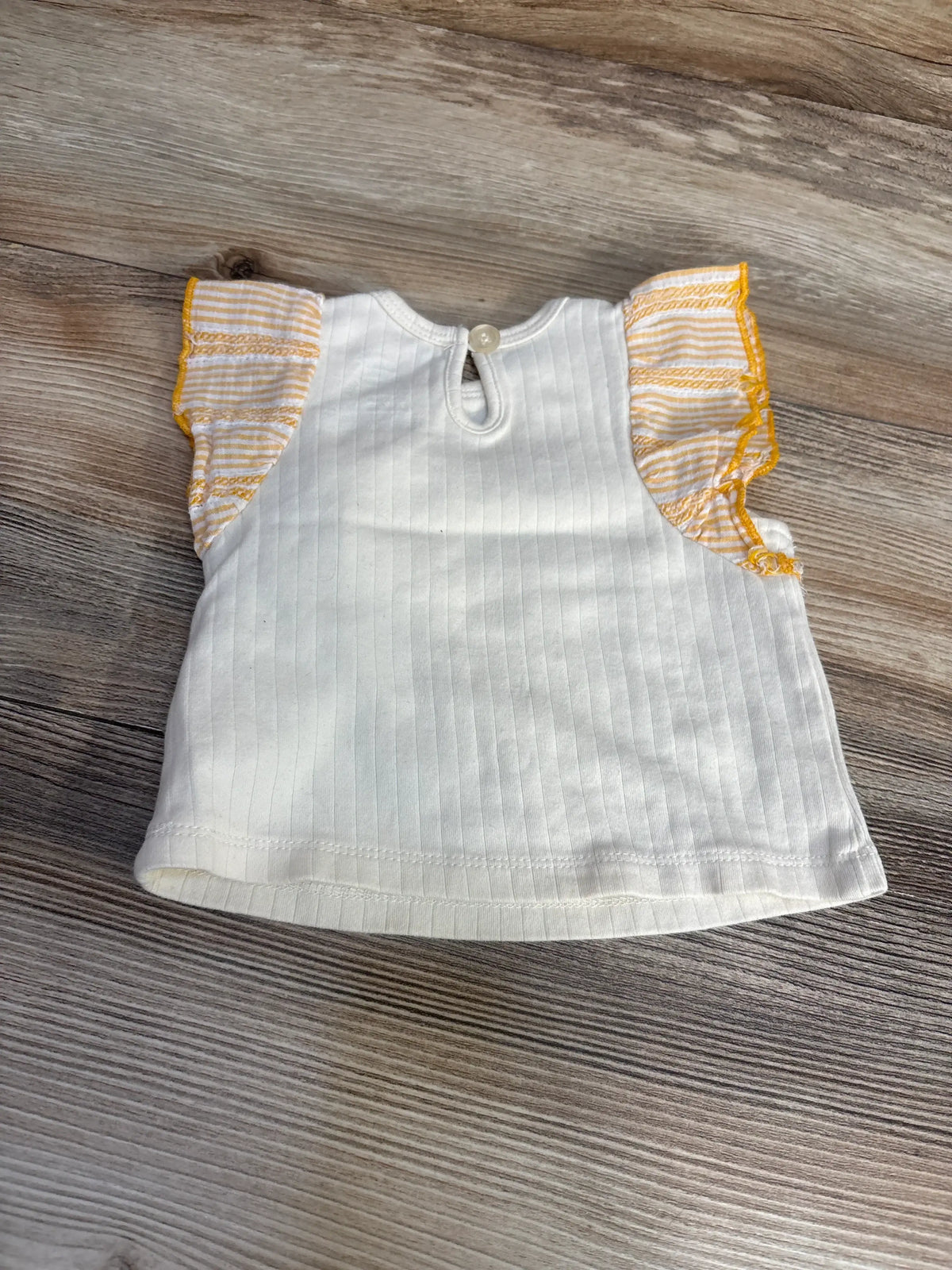 Flat lay of cream Exersaucer baby shirt with ribbed fabric and yellow-striped ruffle sleeves on wood background