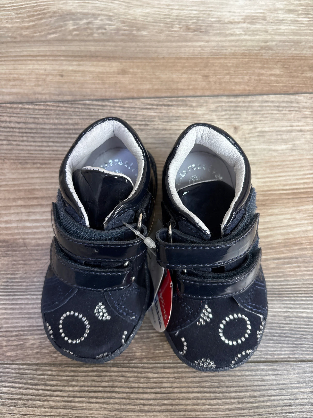 Pair of navy blue baby shoes with silver rhinestone circle design on wood floor