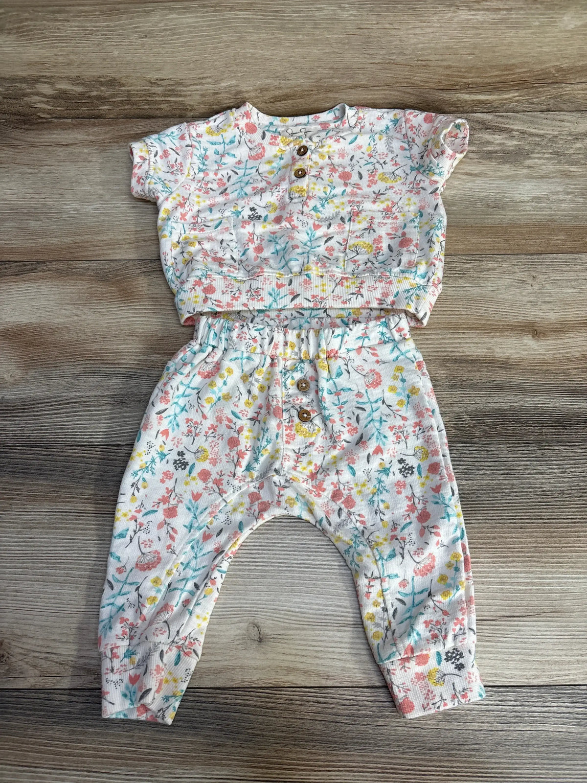 Flat lay of baby two-piece floral shirt and pants with wooden buttons, elastic waist and ribbed cuffs on wood background