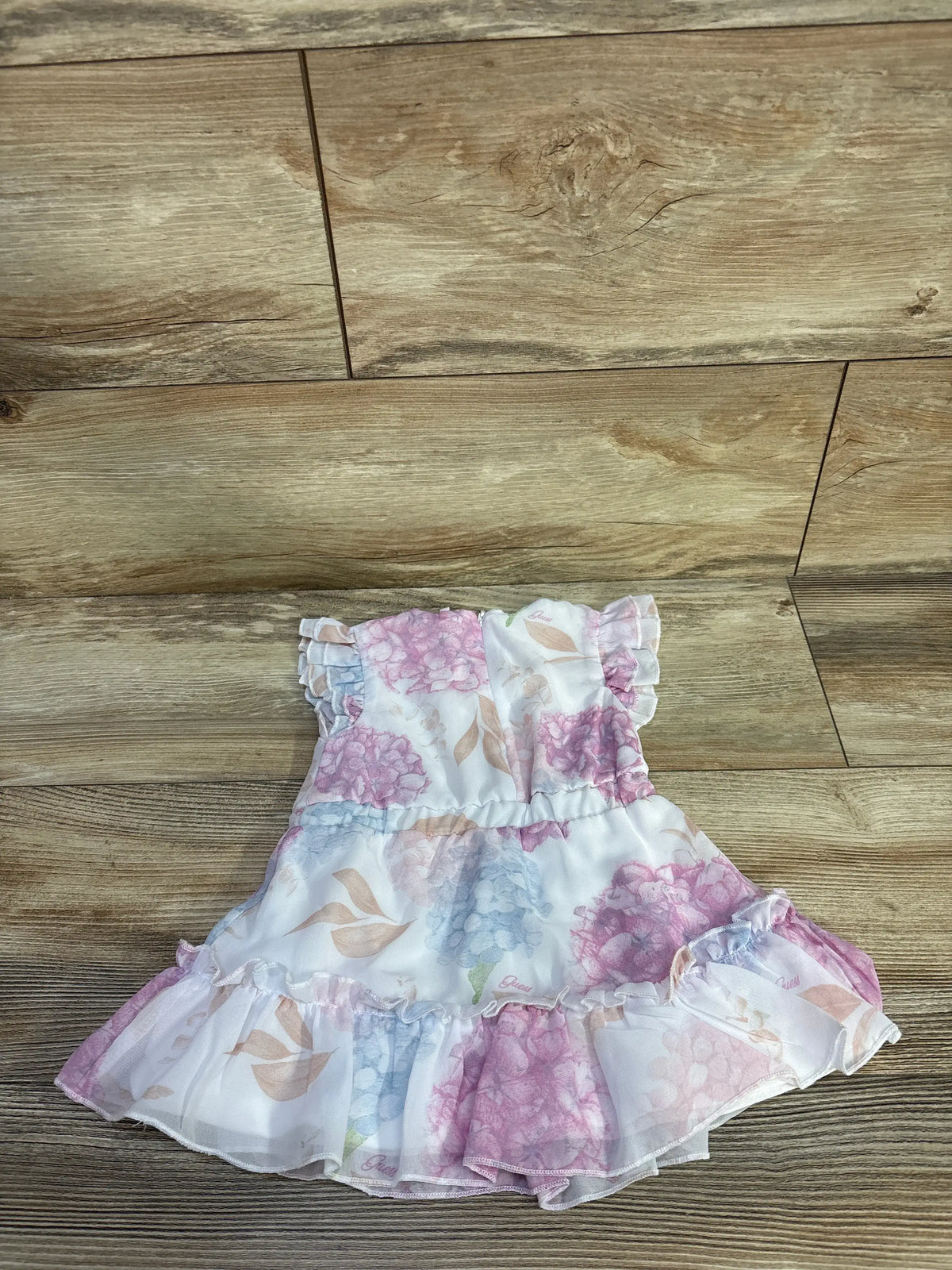 Front view of white Guess floral tulle dress showcasing pink, lilac, and beige floral print with ruffled sleeves on wood flooring