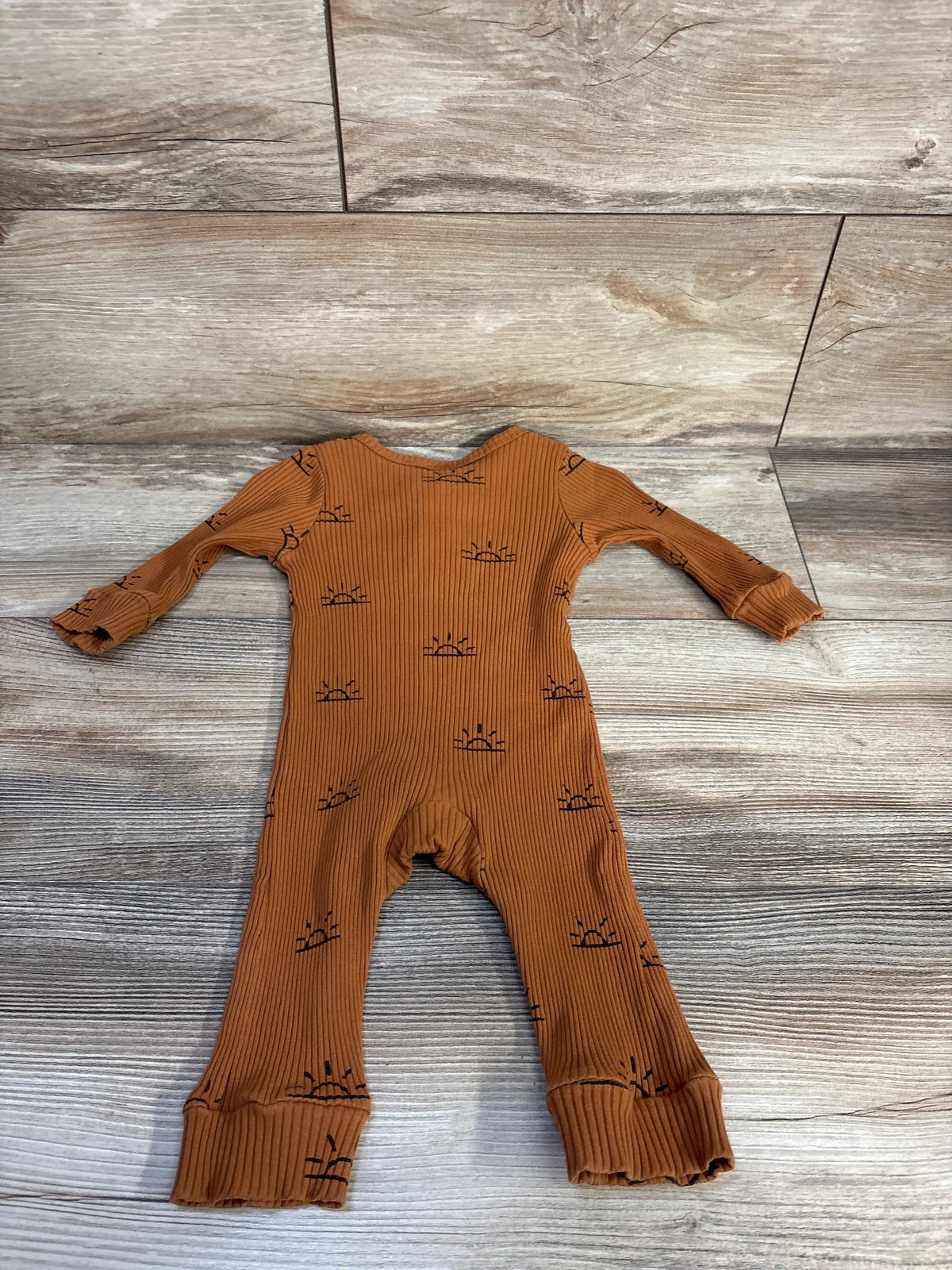Flat lay of brown ribbed henley coverall with black sun print, long sleeves and rolled cuffs on wood background