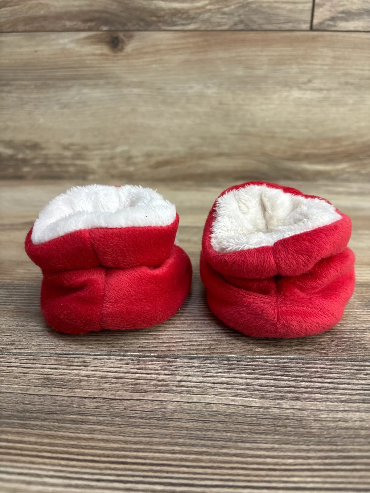 Red and white plush baby booties, soft holiday-themed infant shoes on wood floor