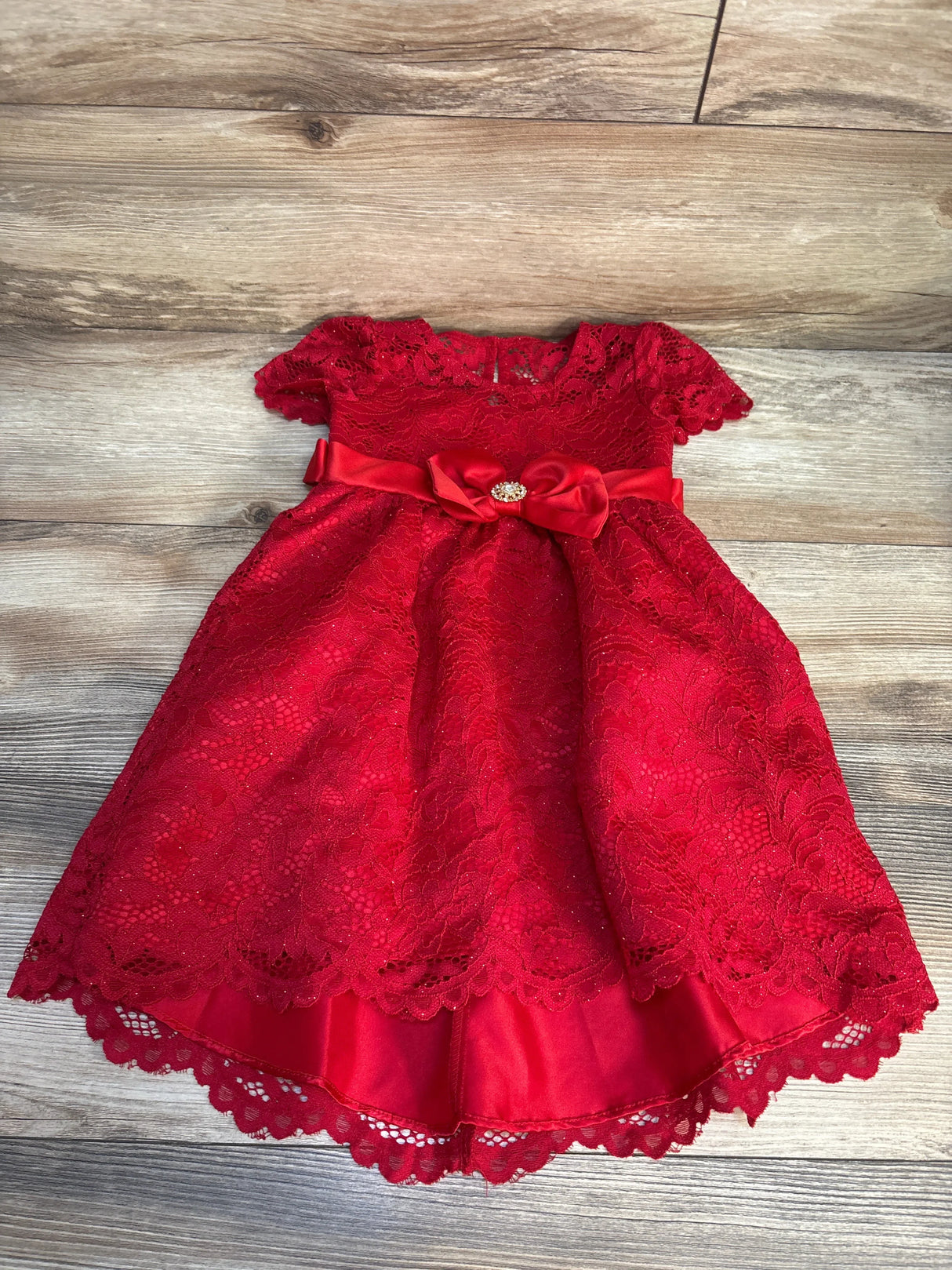 Red lace baby dress with short sleeves, satin bow, and jeweled accent on wooden floor