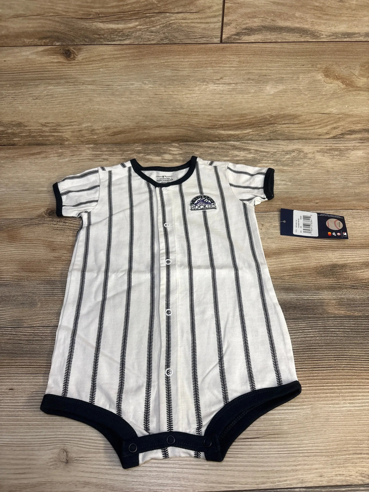 Flat lay of white Colorado Rockies pinstripe romper 24m showcasing front snaps, navy trim, embroidered Rockies logo on wood