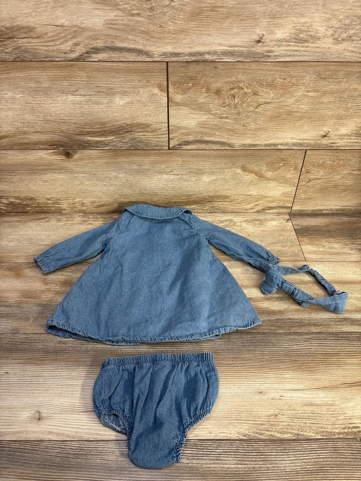 Back view of Minibean 3pc blue denim dress set showing collared long-sleeve dress, bloomers and headband on wood flooring