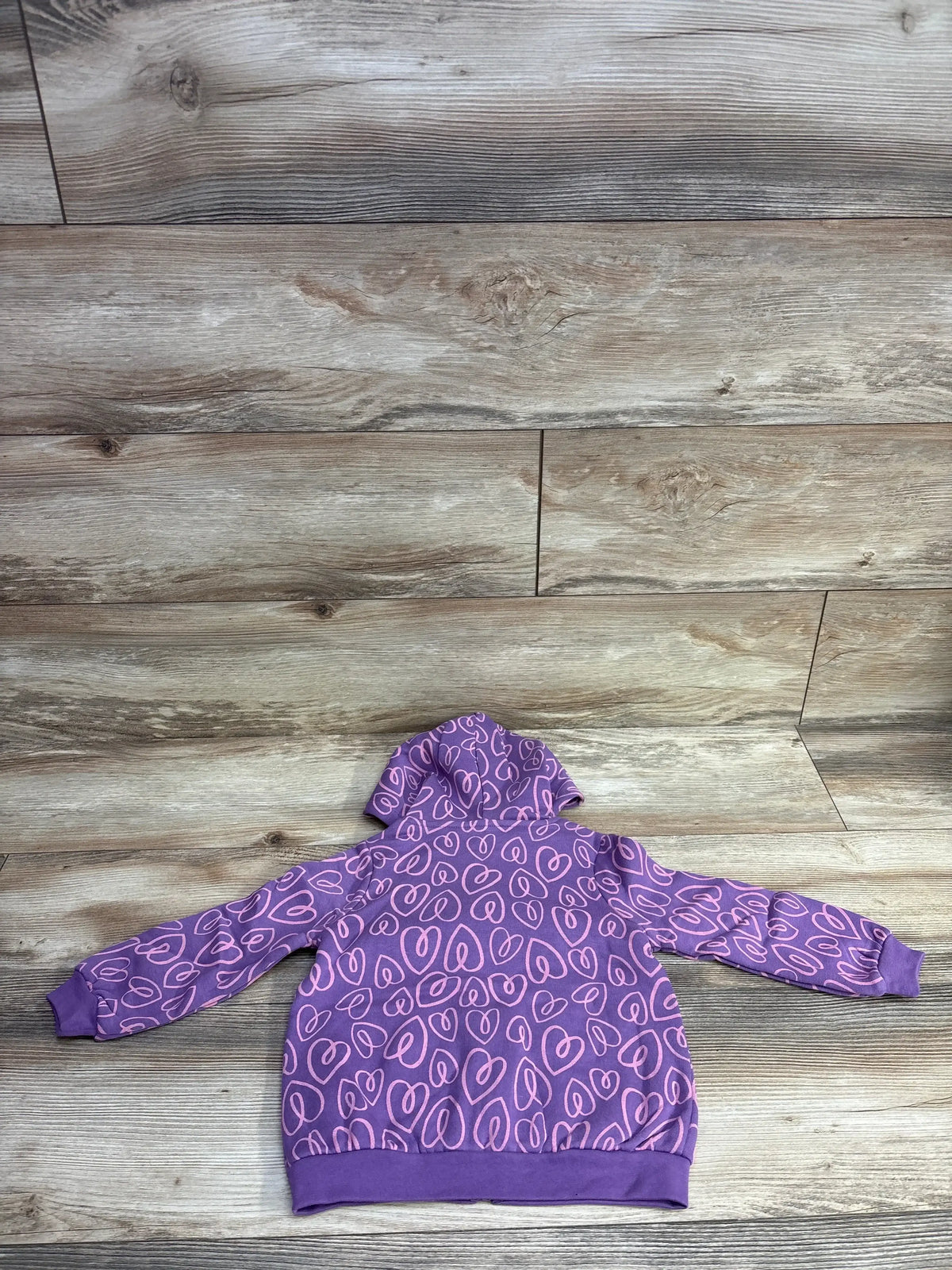 Purple toddler hoodie with pink heart pattern laid flat on wooden floor