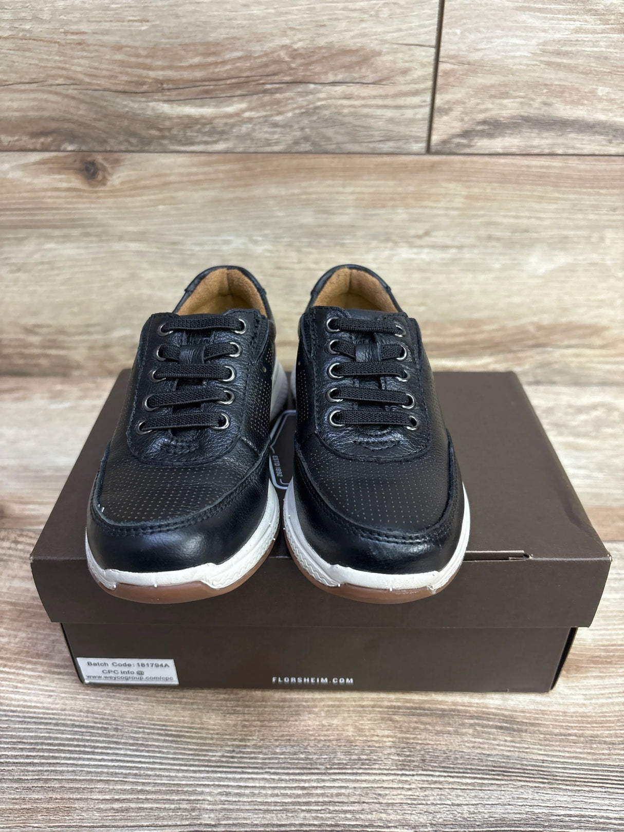 Black kids' athletic sneakers with white soles on a shoebox, wood background
