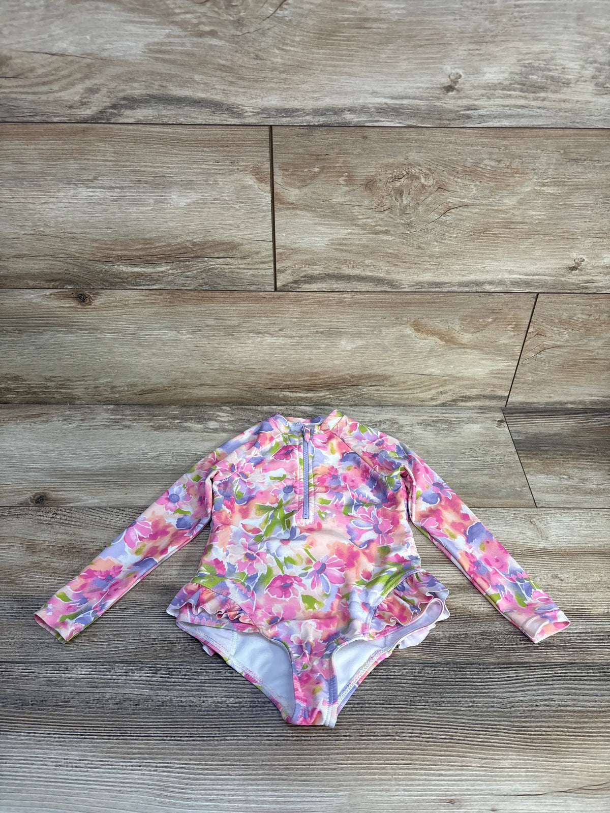 Front view of Banana Boat 1pc rash guard swimsuit with long sleeves, pink floral print, and front zipper on wood background