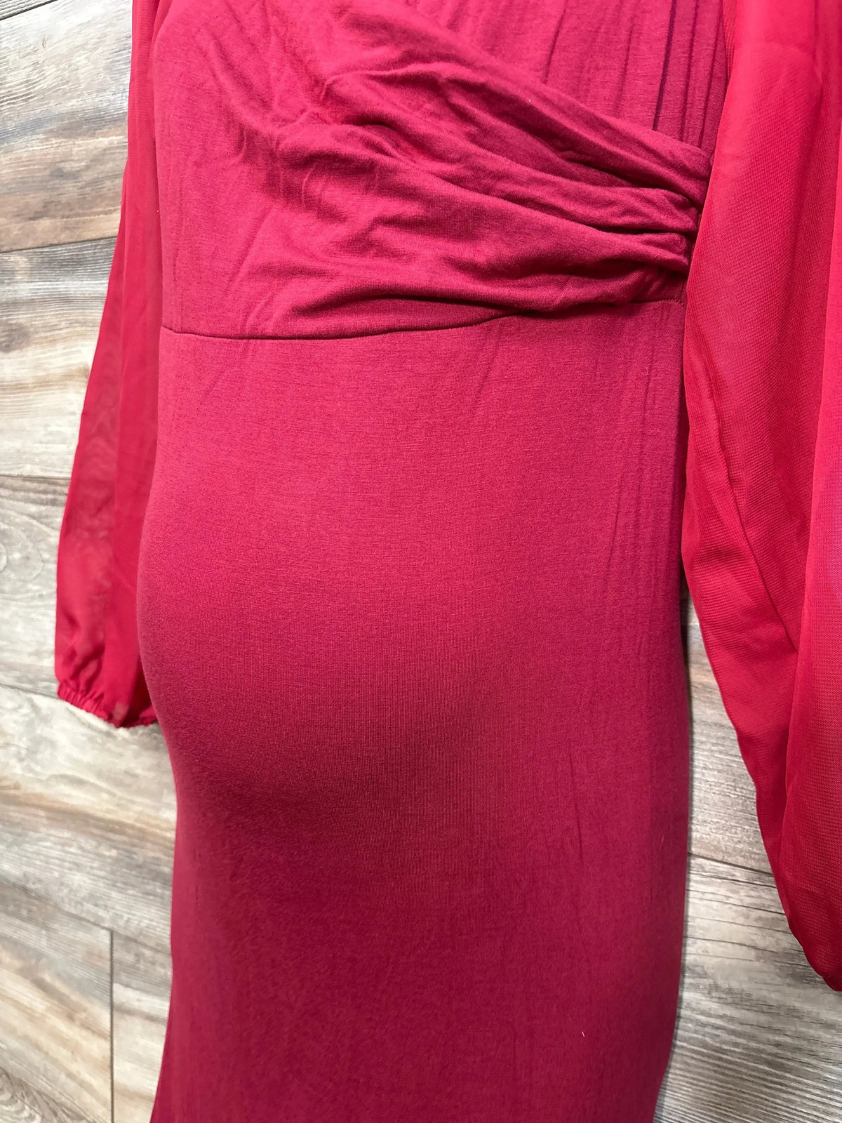 Side close-up of red maternity mermaid dress showing ruched bodice, chiffon long sleeve and fitted skirt on wood background