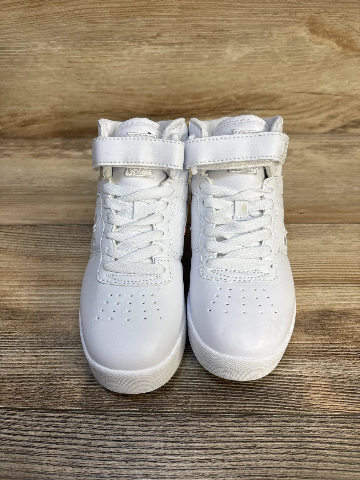 Pair of white kids high-top sneakers with velcro straps on wood background