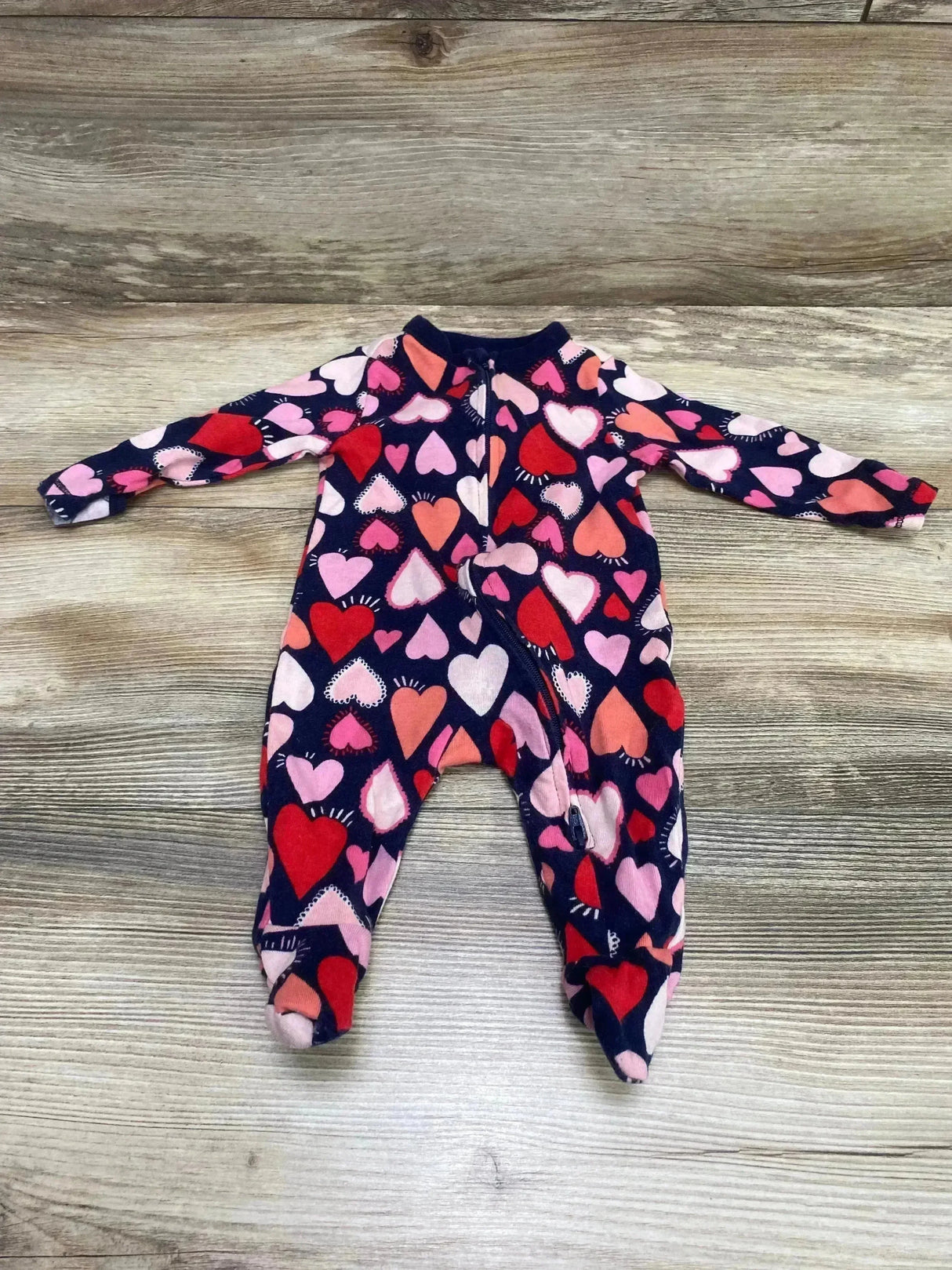Top down view of Old Navy navy footed baby sleeper showing multicolor heart print and front zipper on light wood background