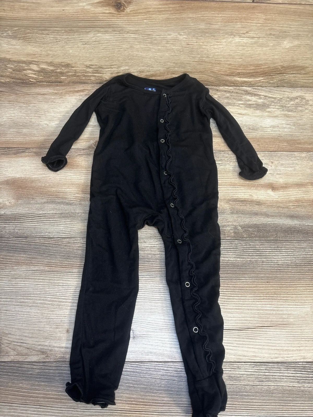Black long sleeve baby romper with ruffle snaps, laid flat on wood background