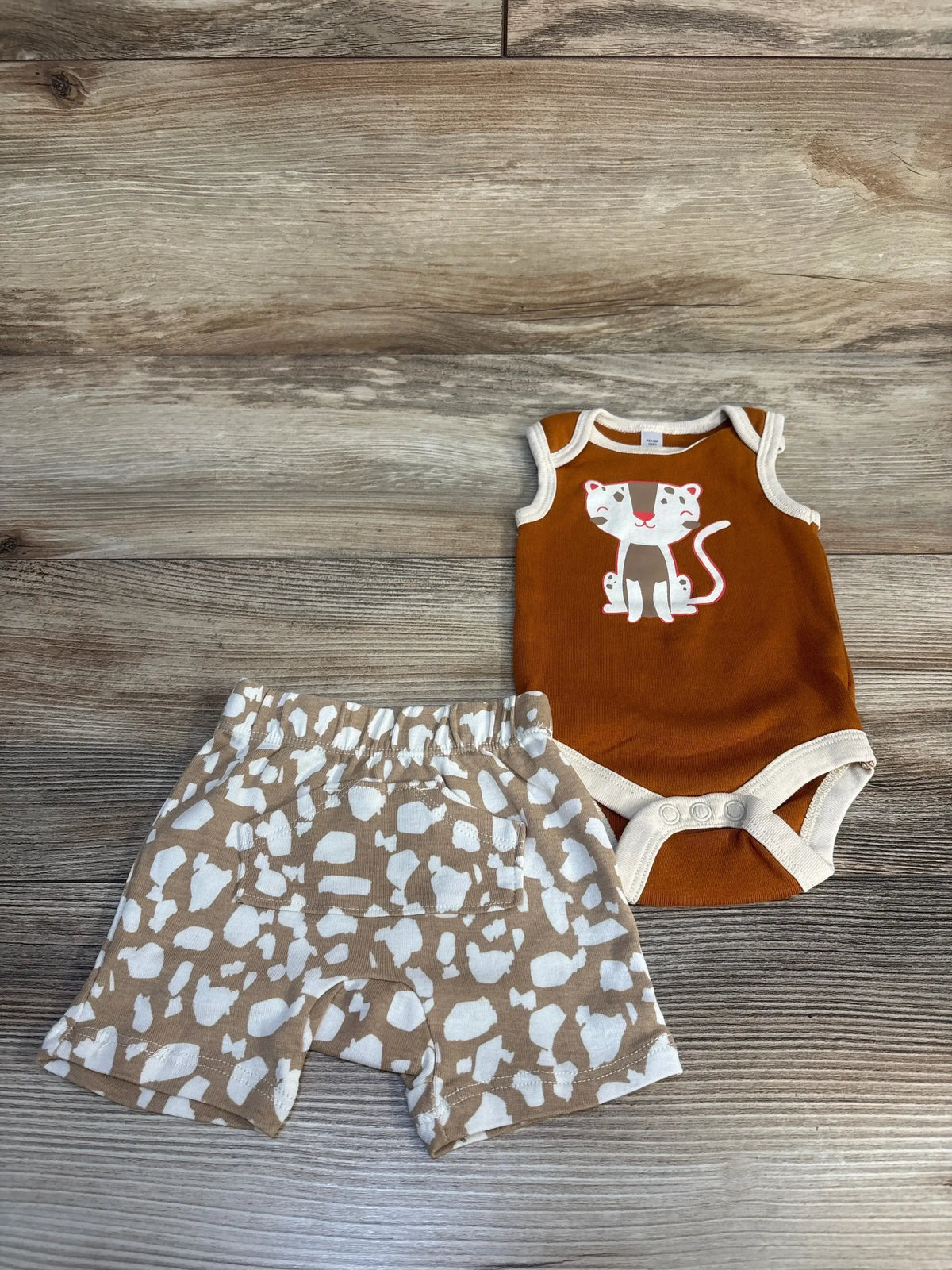 Baby outfit with brown cat print onesie and patterned shorts on wooden background