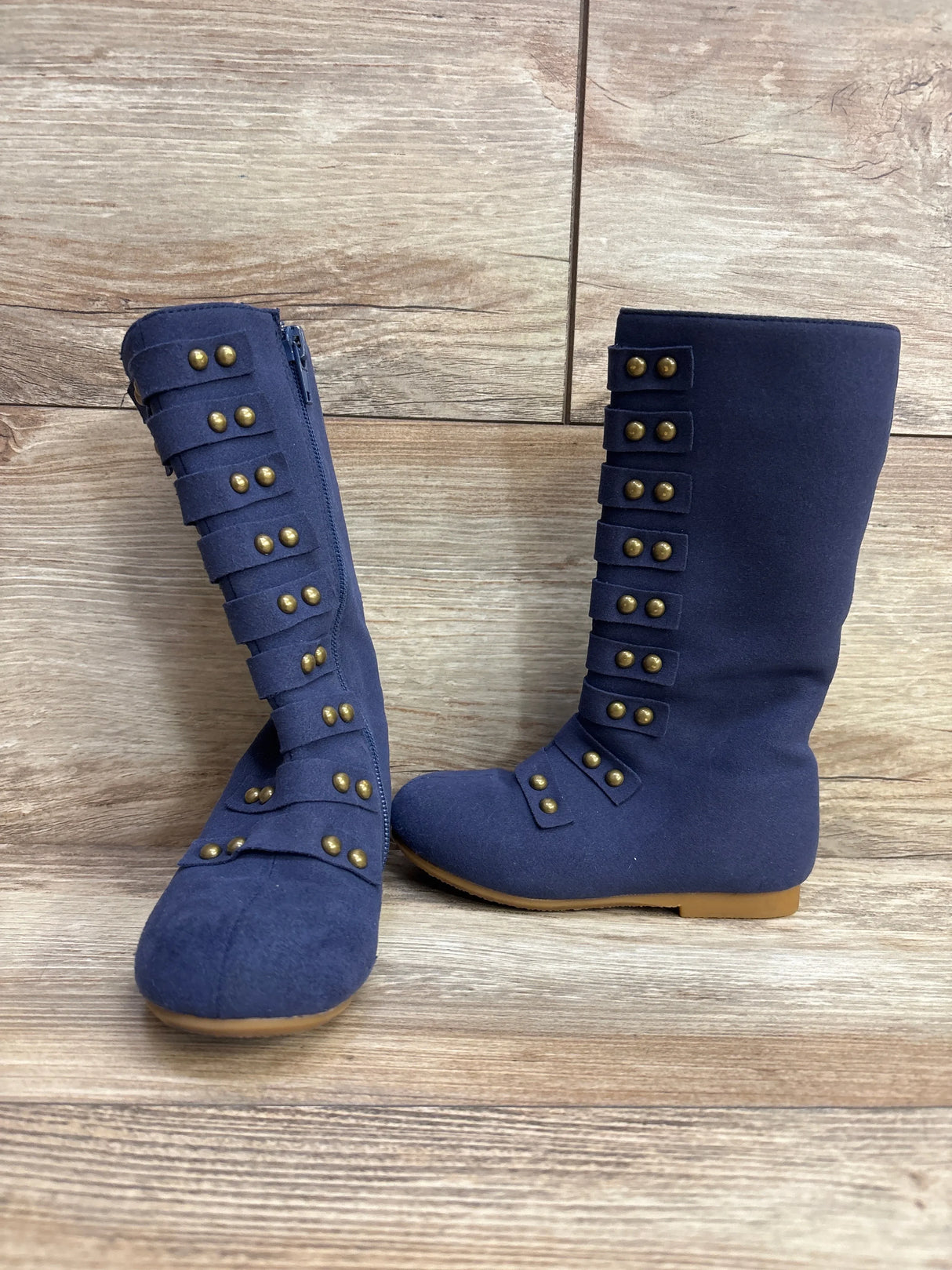 Pair of navy blue kids boots with bronze stud details on wooden floor background