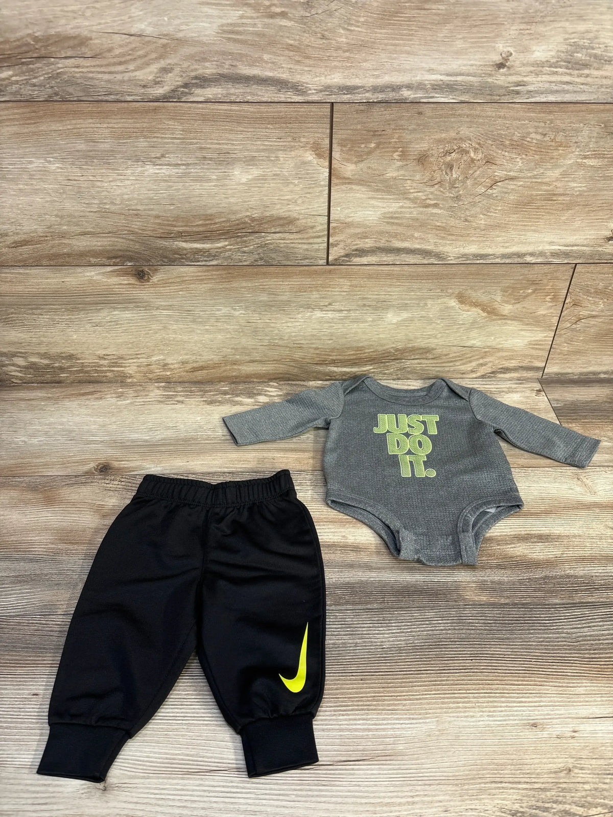 Flat lay of grey long sleeve Nike bodysuit with JUST DO IT text and black joggers with yellow Nike swoosh on wood floor