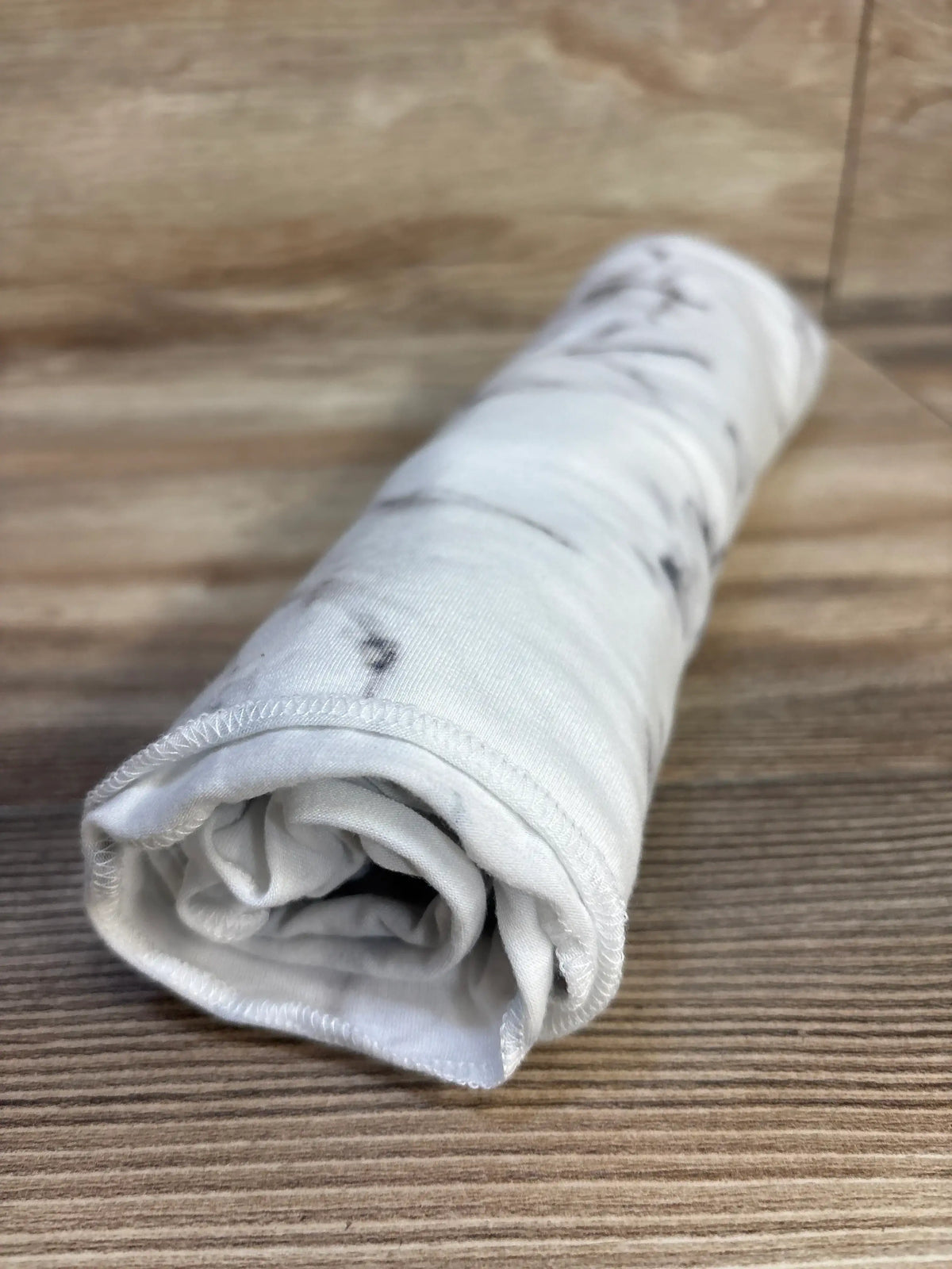 Close-up of rolled Copper Pearl knit swaddle blanket in marble white showing soft knit texture and gray marbling on wooden floor