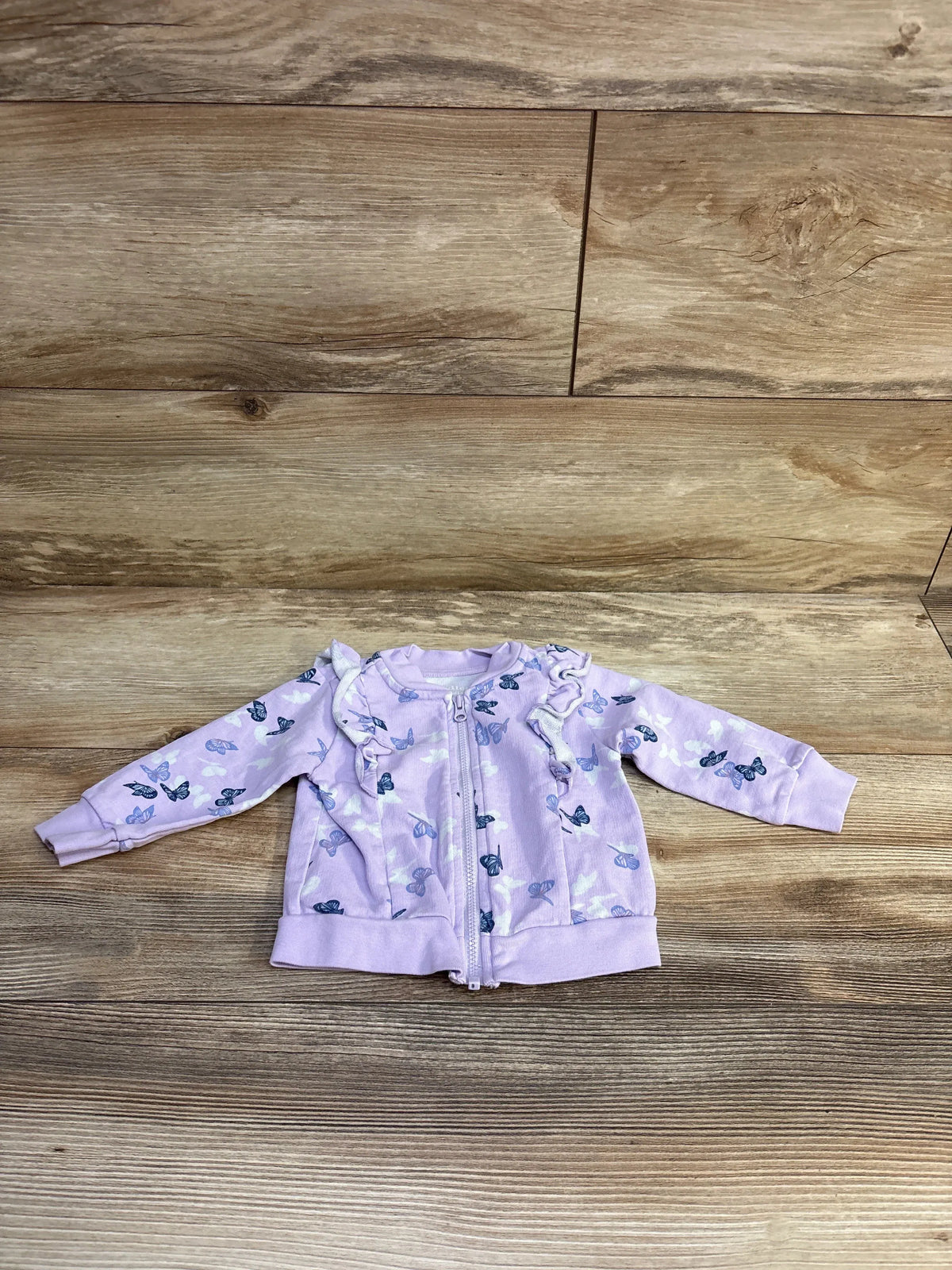 Front flat lay of purple baby zip jacket size 6-9 months with butterfly print and ruffle shoulders on wood background