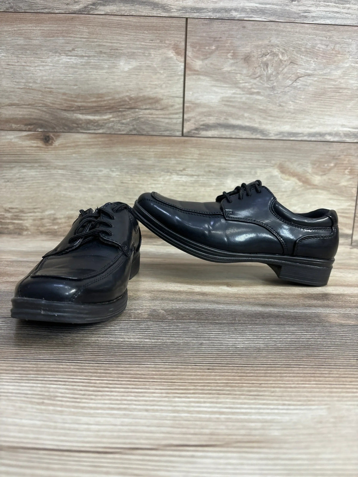 Pair of black leather kids' dress shoes on wooden floor background