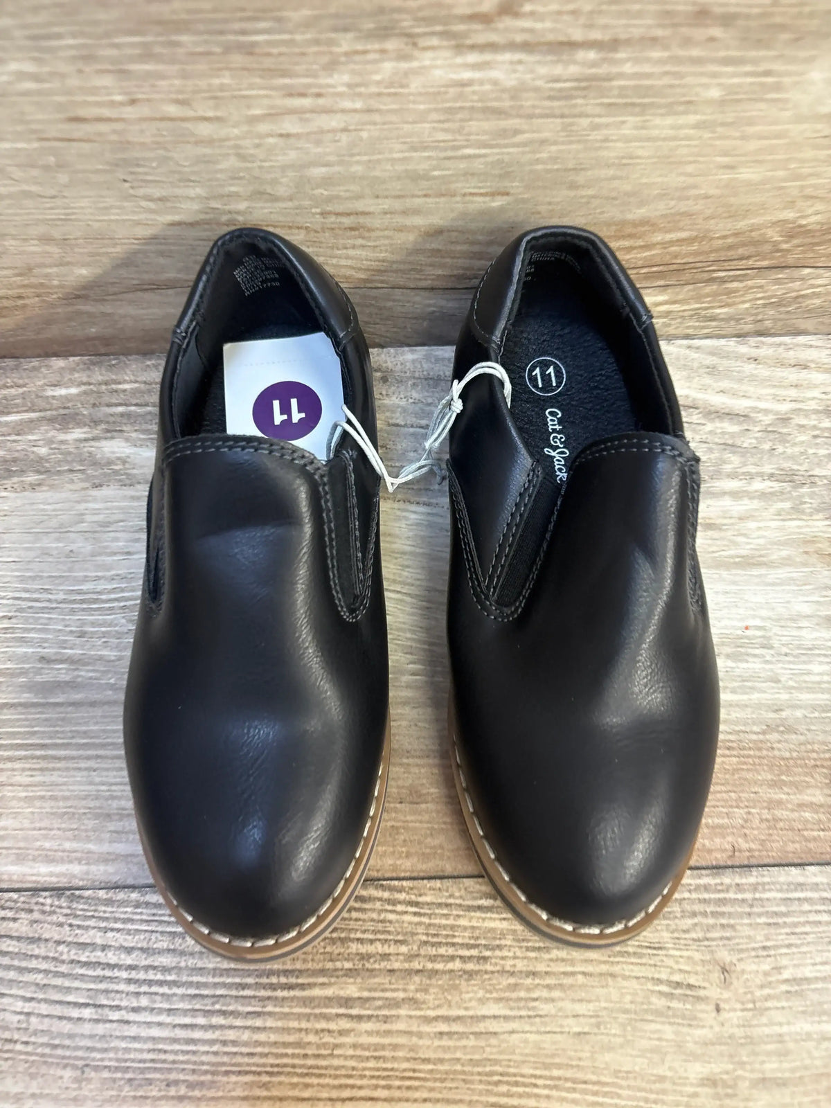 Black slip-on kids dress shoes, size 11, displayed on wood floor