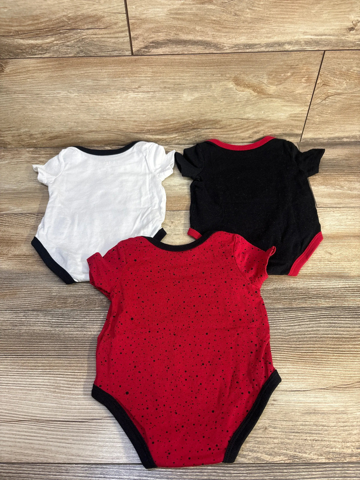 Front view of Jordan 3-pack bodysuits showcasing short sleeves and curved leg openings on a wood floor