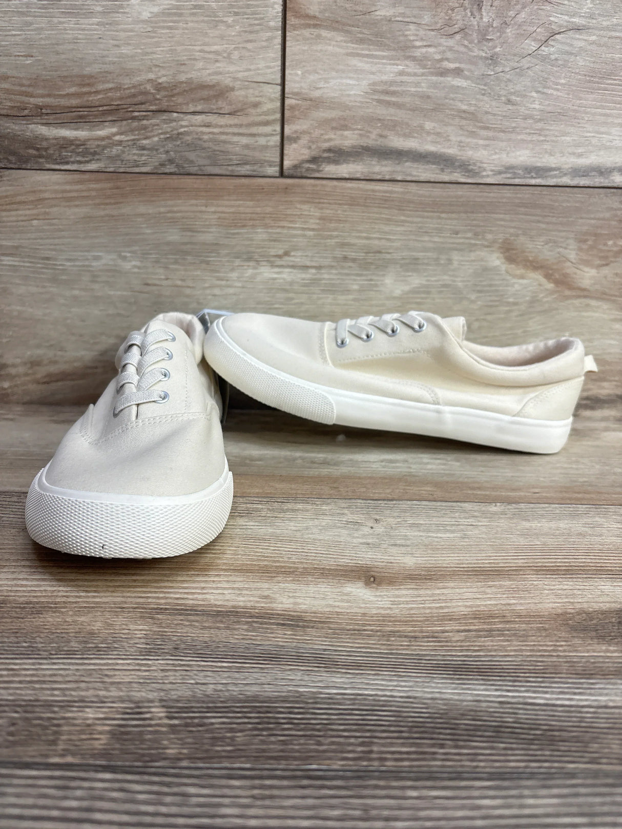 Pair of cream canvas sneakers with white rubber soles on wood floor