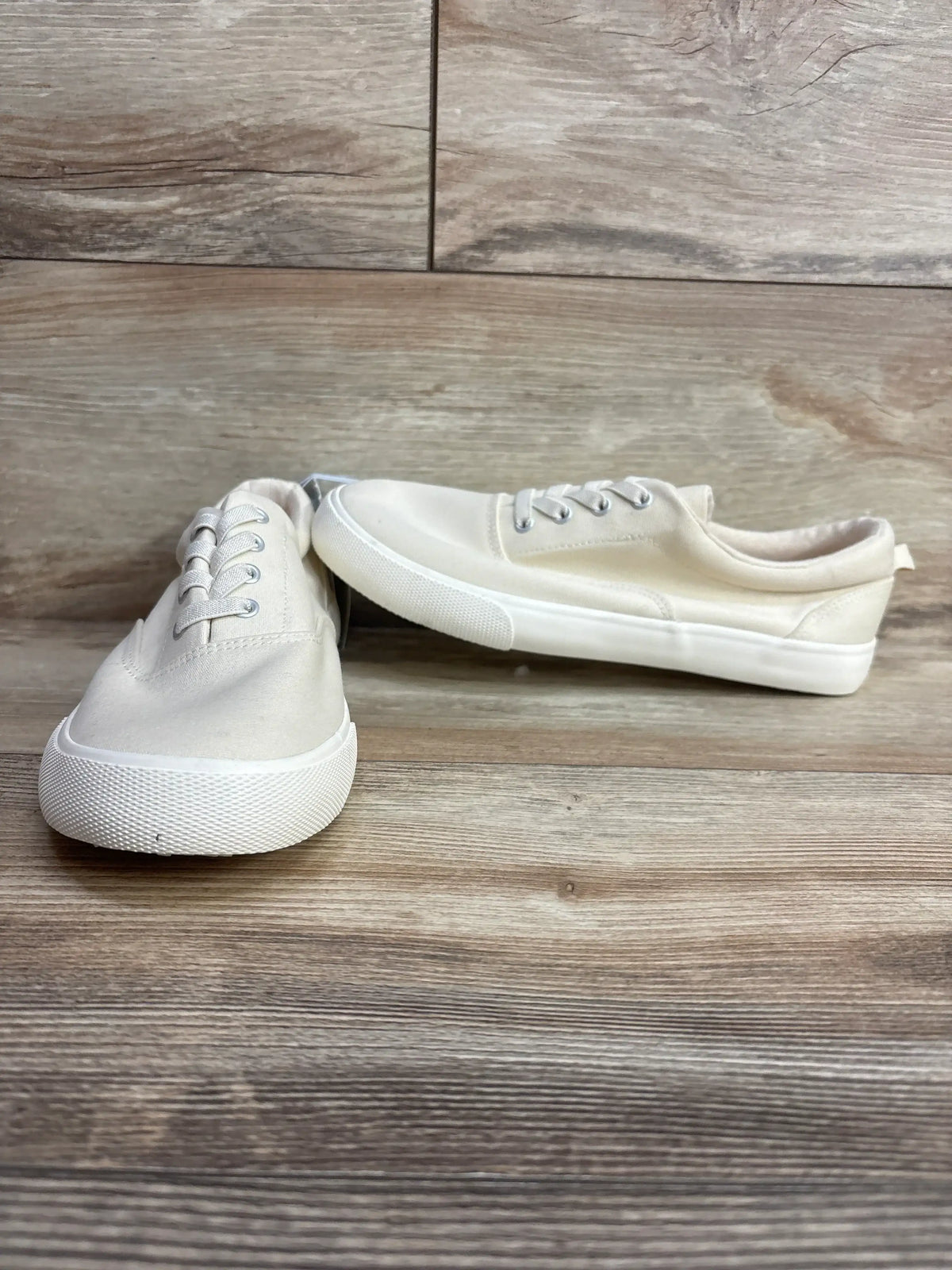Pair of cream canvas sneakers with white rubber soles on wood floor
