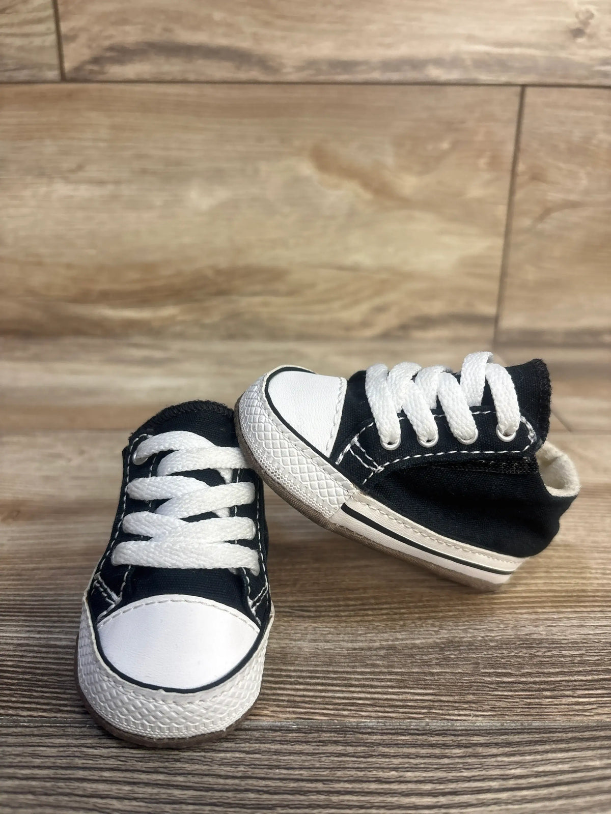 Front and side views of a pair of black Converse All Star Cribster Easy-On shoes with white toe caps on a wood floor