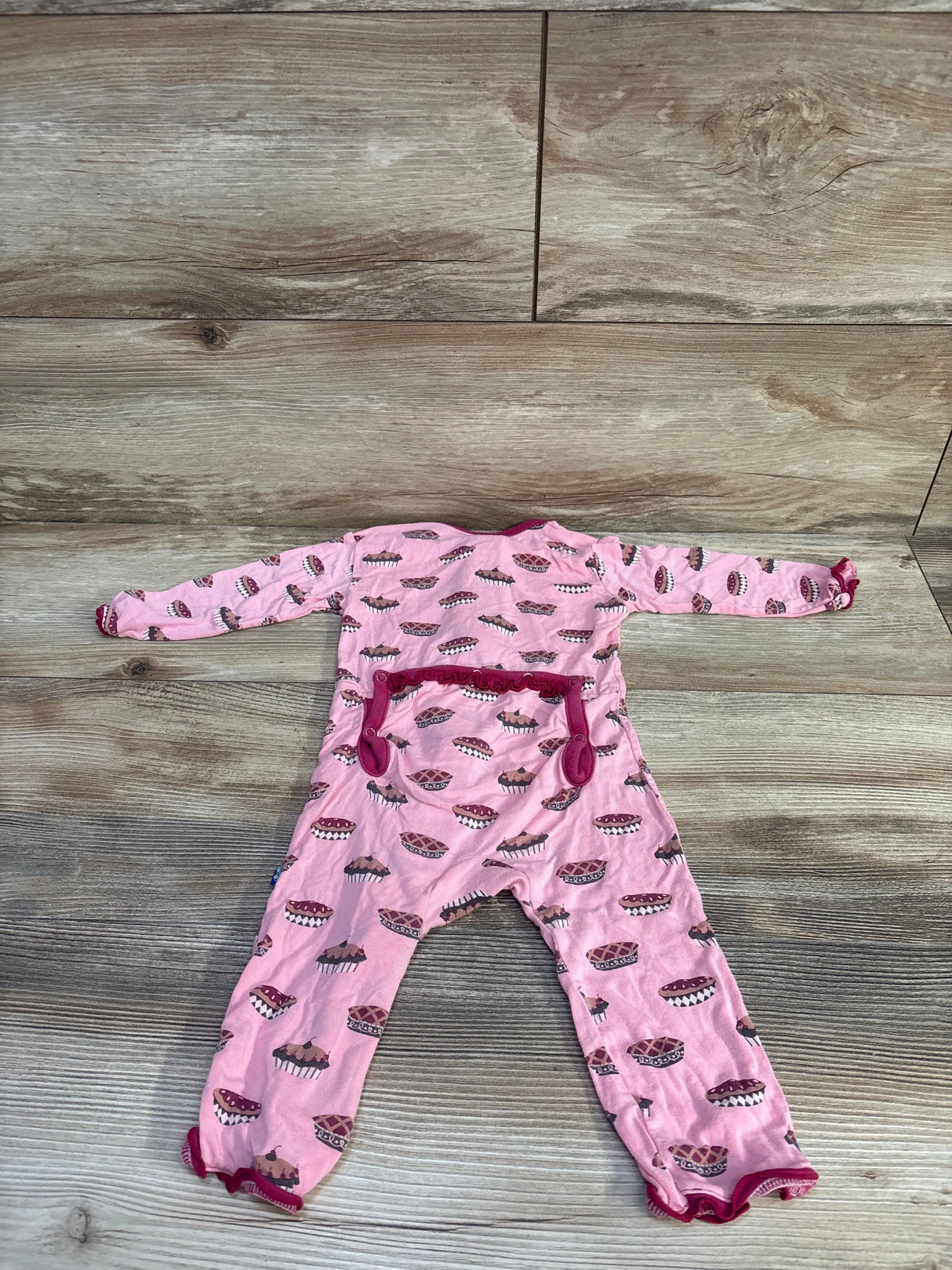 Flat-lay of pink Kickee Pants bamboo zip coverall with muffin print and ruffle trim, size 3-6 months, on wood floor